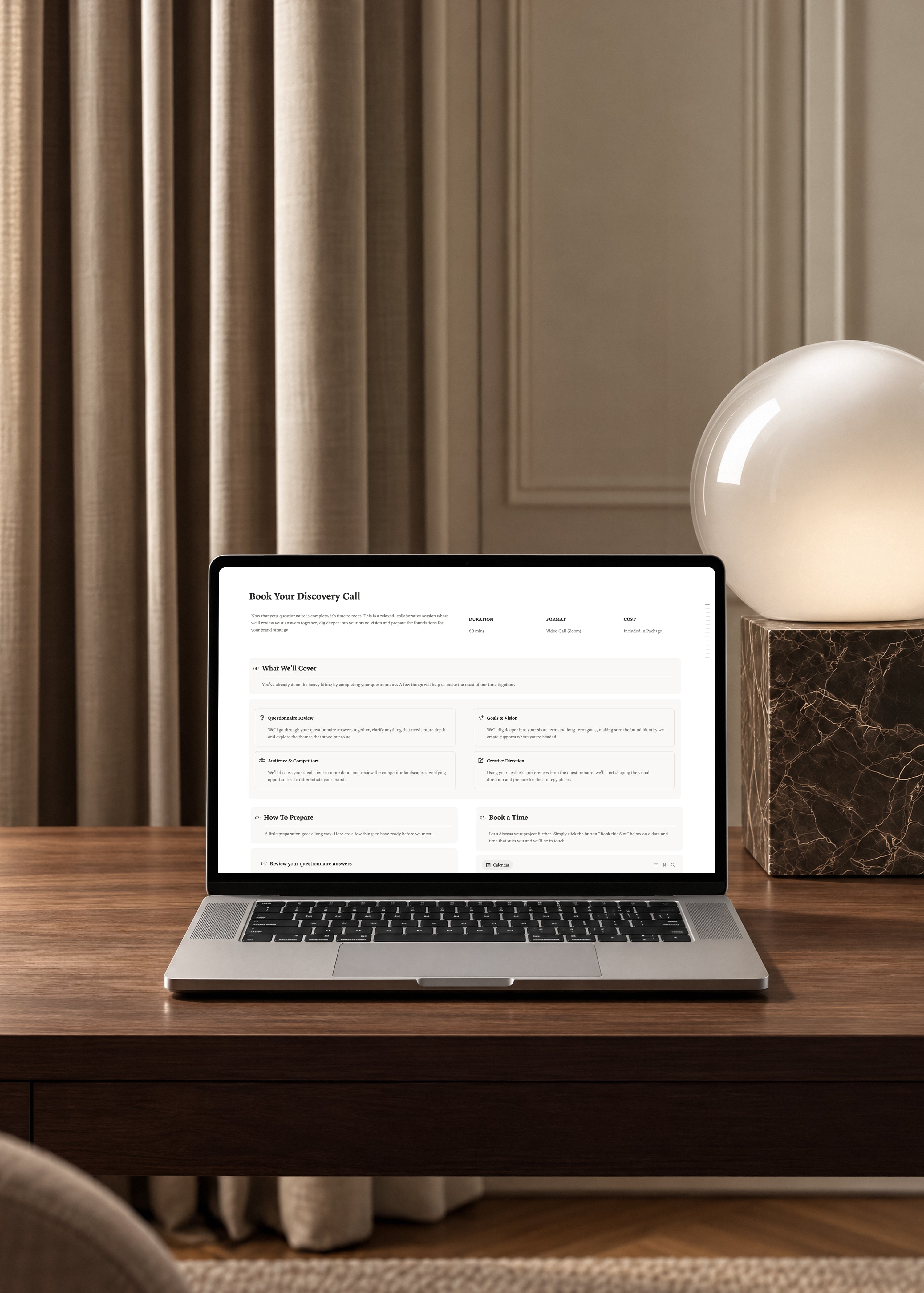 Notion client portal Book Your Discovery Call page on a laptop, showing call details and what to cover, on a walnut desk beside a glowing globe lamp.