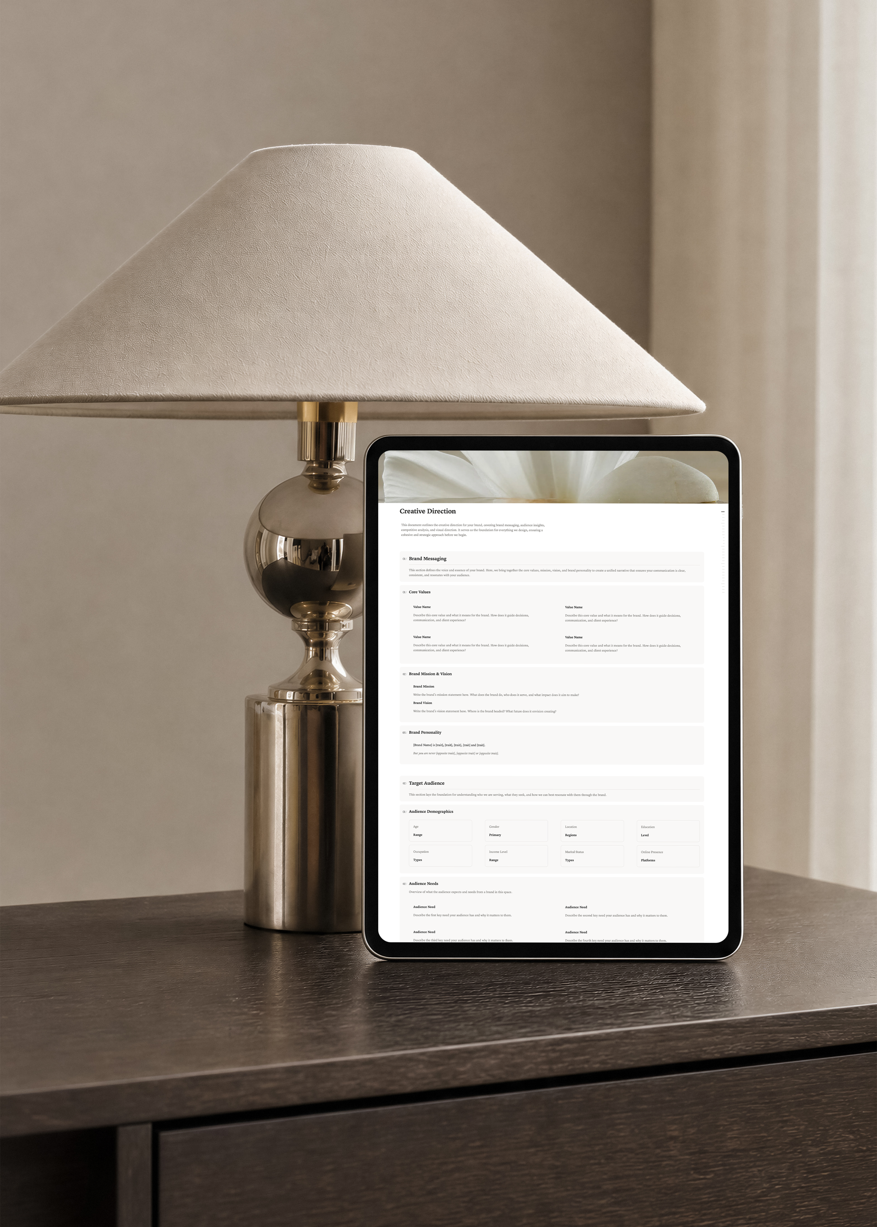 Notion client portal Creative Direction page on an iPad, showing brand messaging, core values and target audience sections beside a brass table lamp.