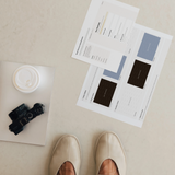 Printed pages from a Notion brand identity client portal showing the Brand Discovery Questionnaire and colour palette, on a stone floor with a camera and coffee.