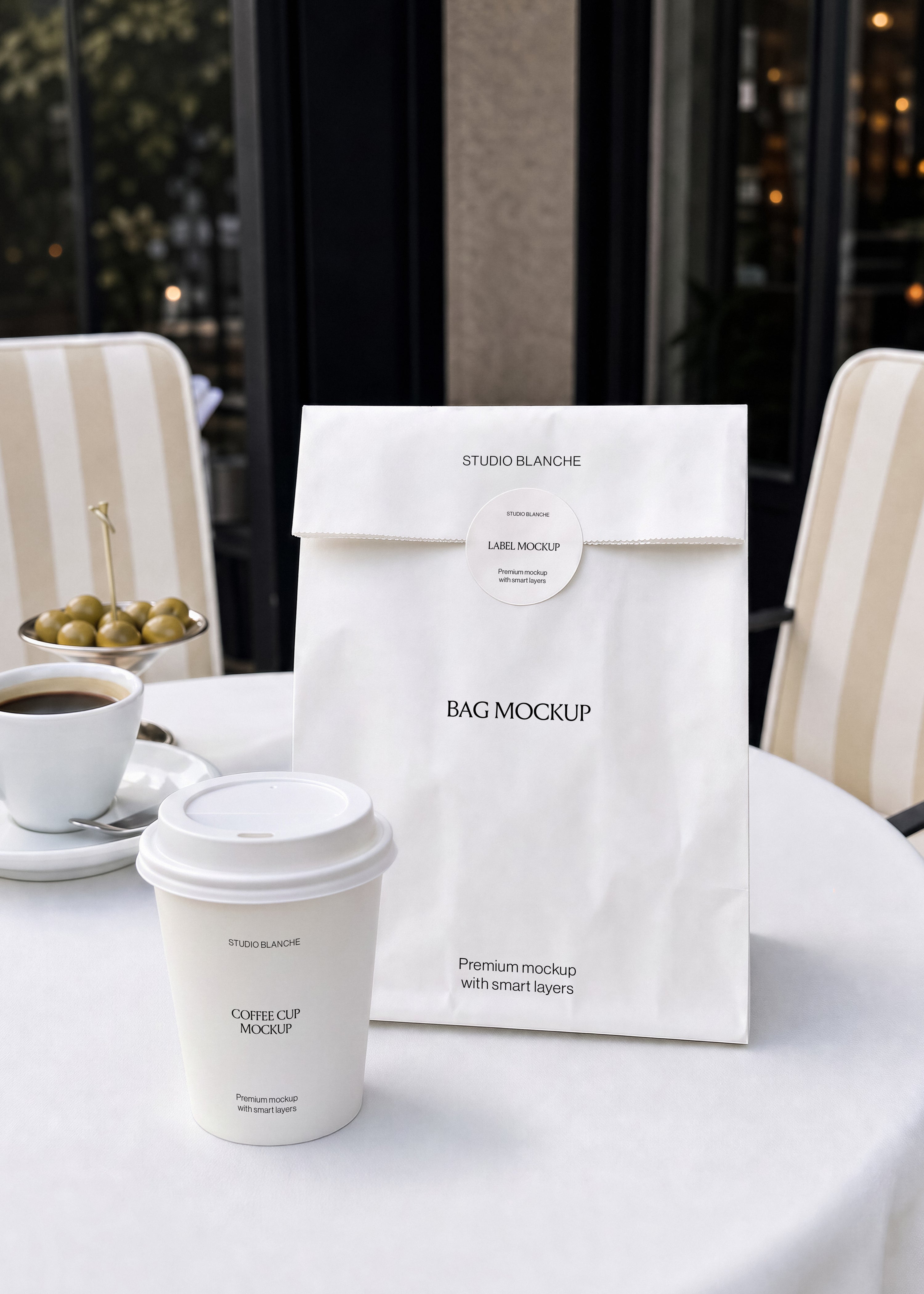 Coffee cup and paper bag mockup with round sticker on white tablecloth, espresso cup and olives, cream striped chairs