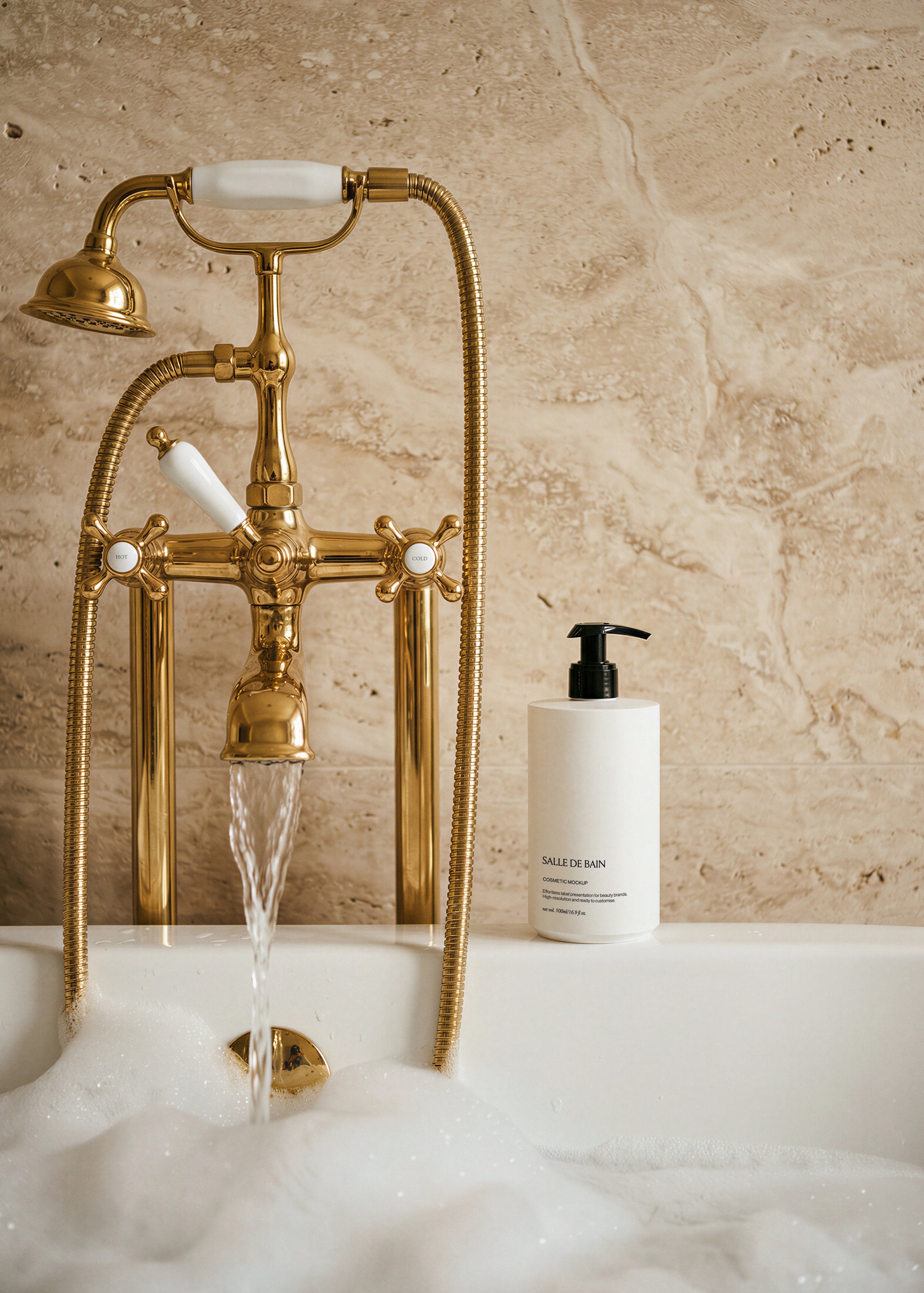 White cosmetic pump bottle mockup with black pump on bathtub edge beside gold telephone tap, foam and travertine wall