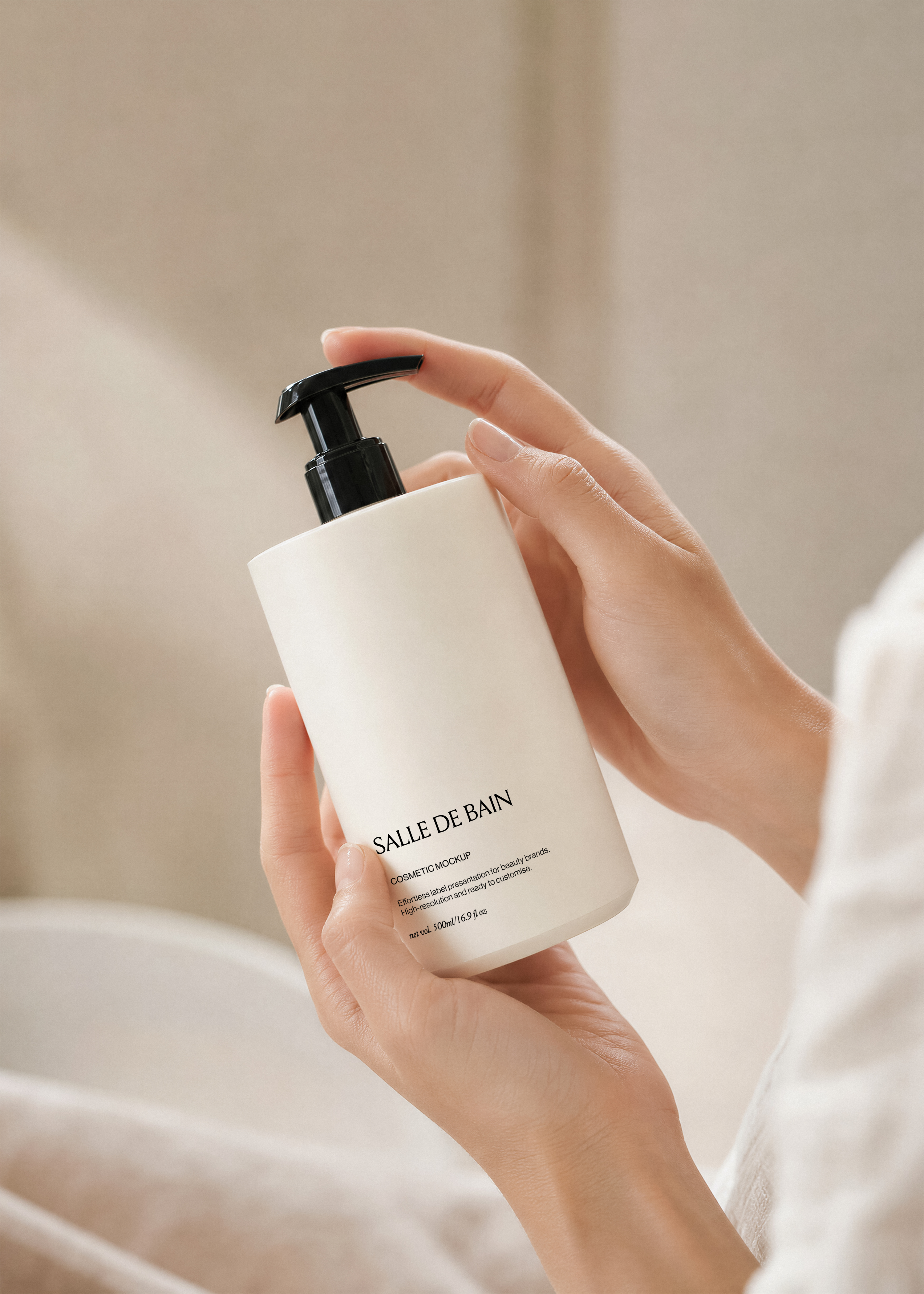 White plastic pump bottle mockup with black pump held in two hands against a soft cream background, minimal editorial styling