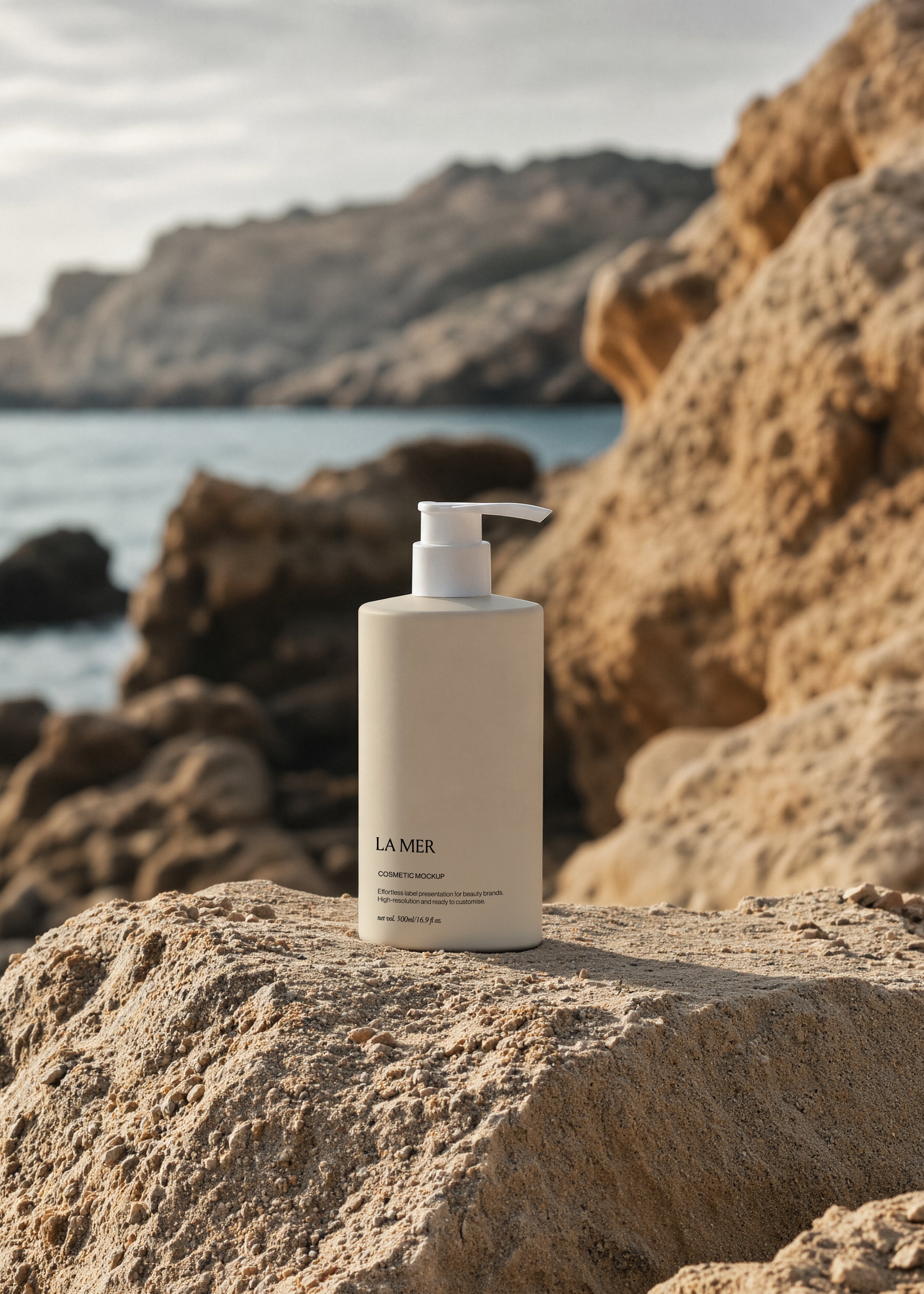 Tall white cosmetic pump bottle standing on bleached limestone rock, warm golden boulders and pale sky in soft focus