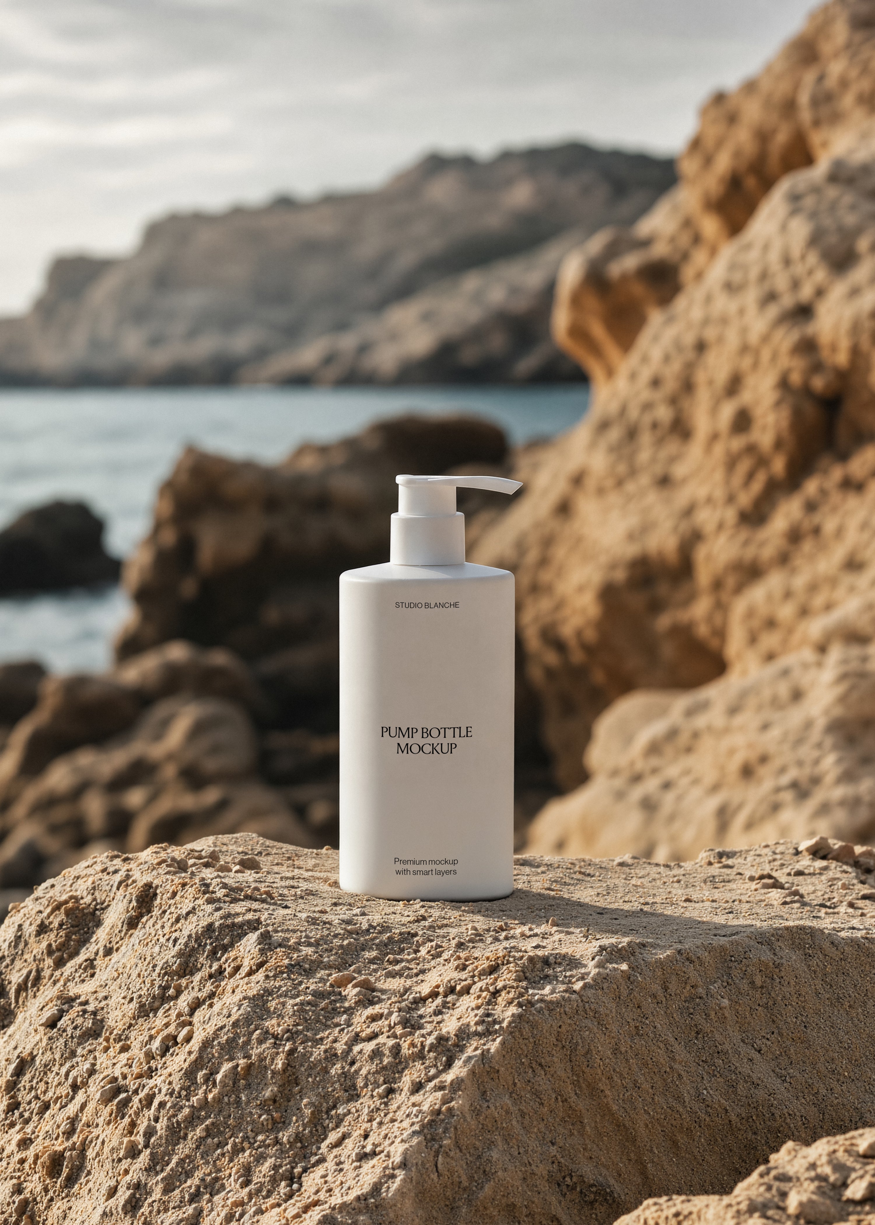 White pump bottle mockup with label on textured coastal rock surface, large warm boulders and blue sky blurred behind