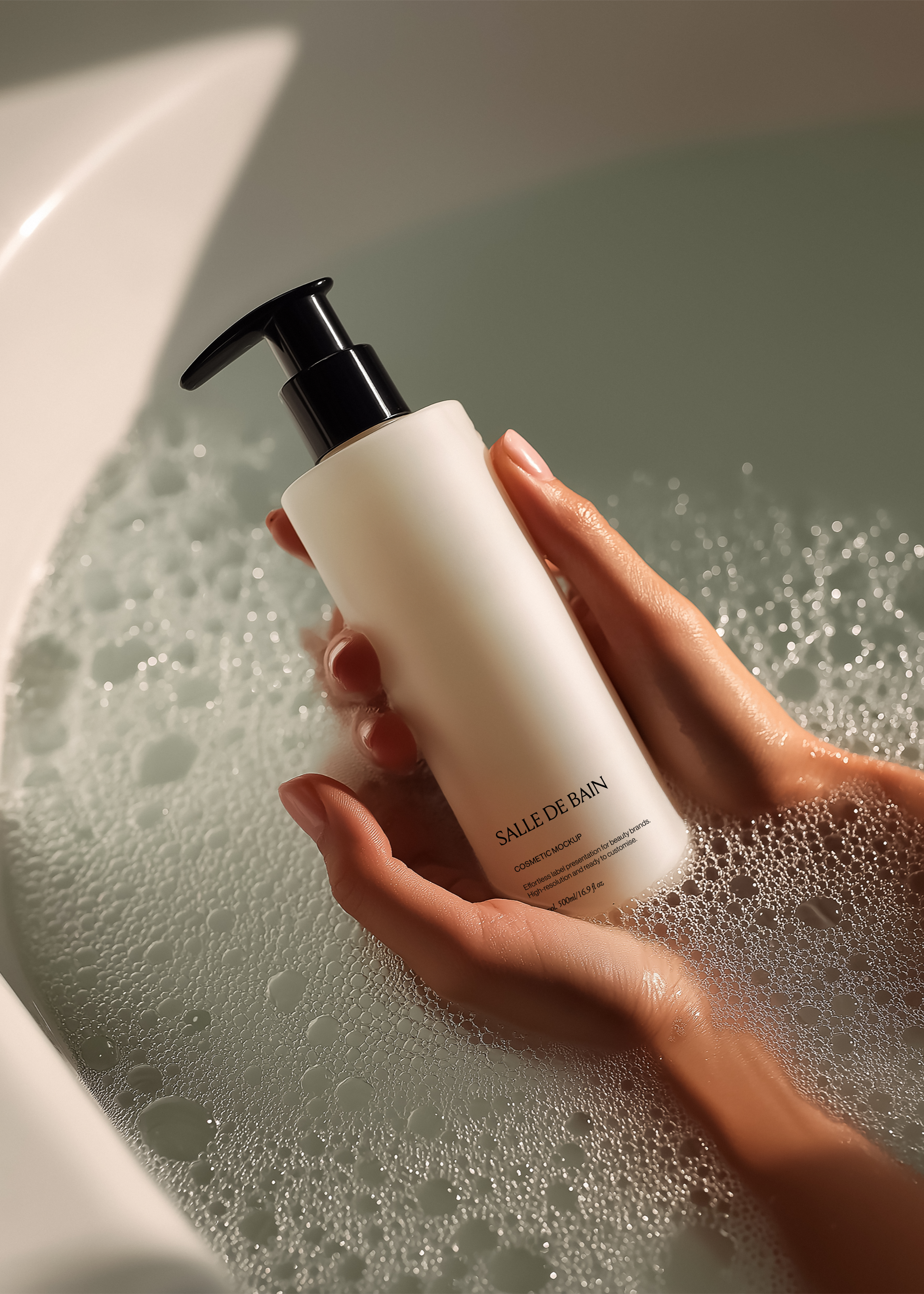 White cosmetic pump bottle with black dispenser cupped in two hands over foamy bath water in soft low light