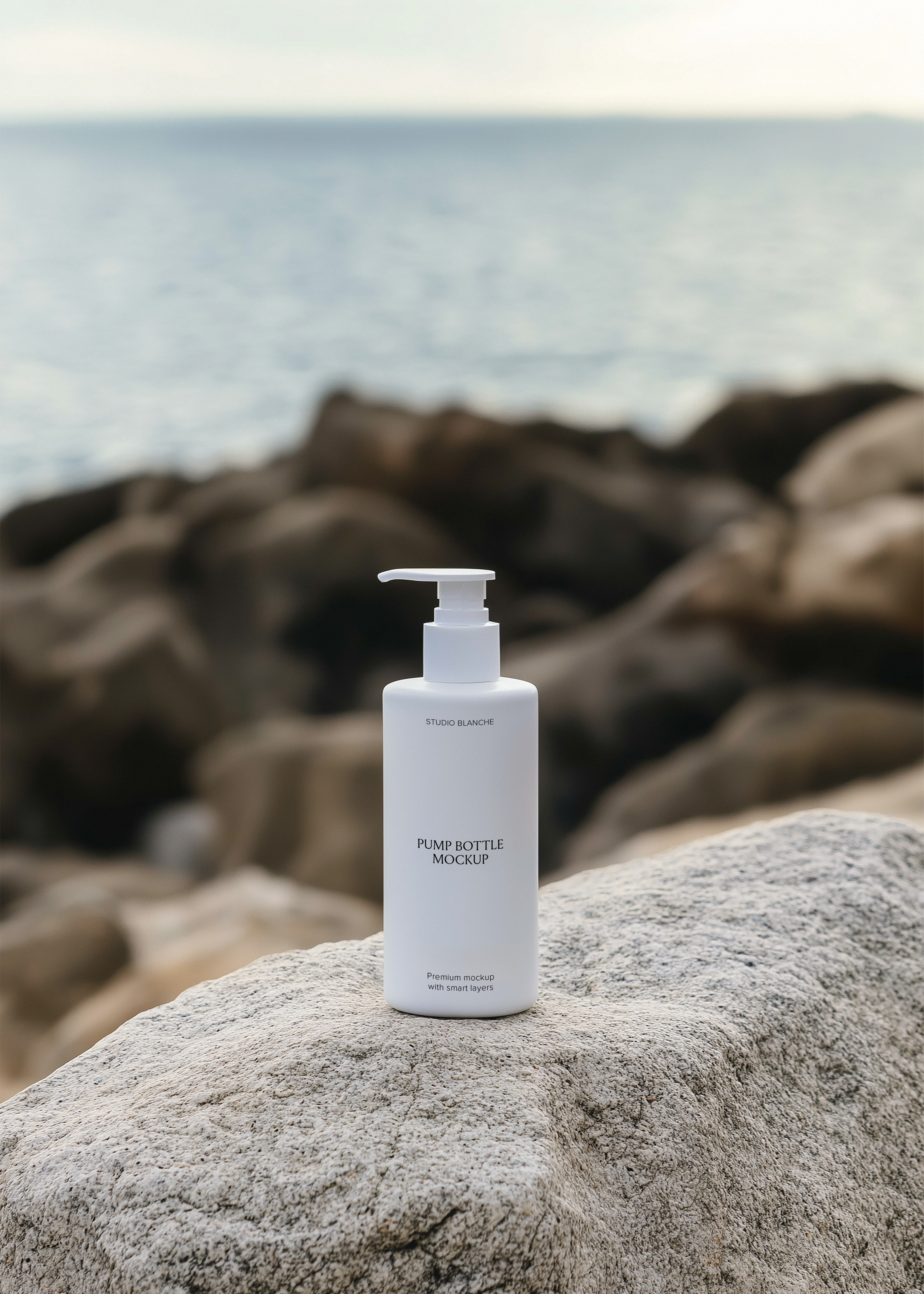 White pump bottle mockup with label on grey granite coastal rock, scattered dark boulders and open sea horizon behind