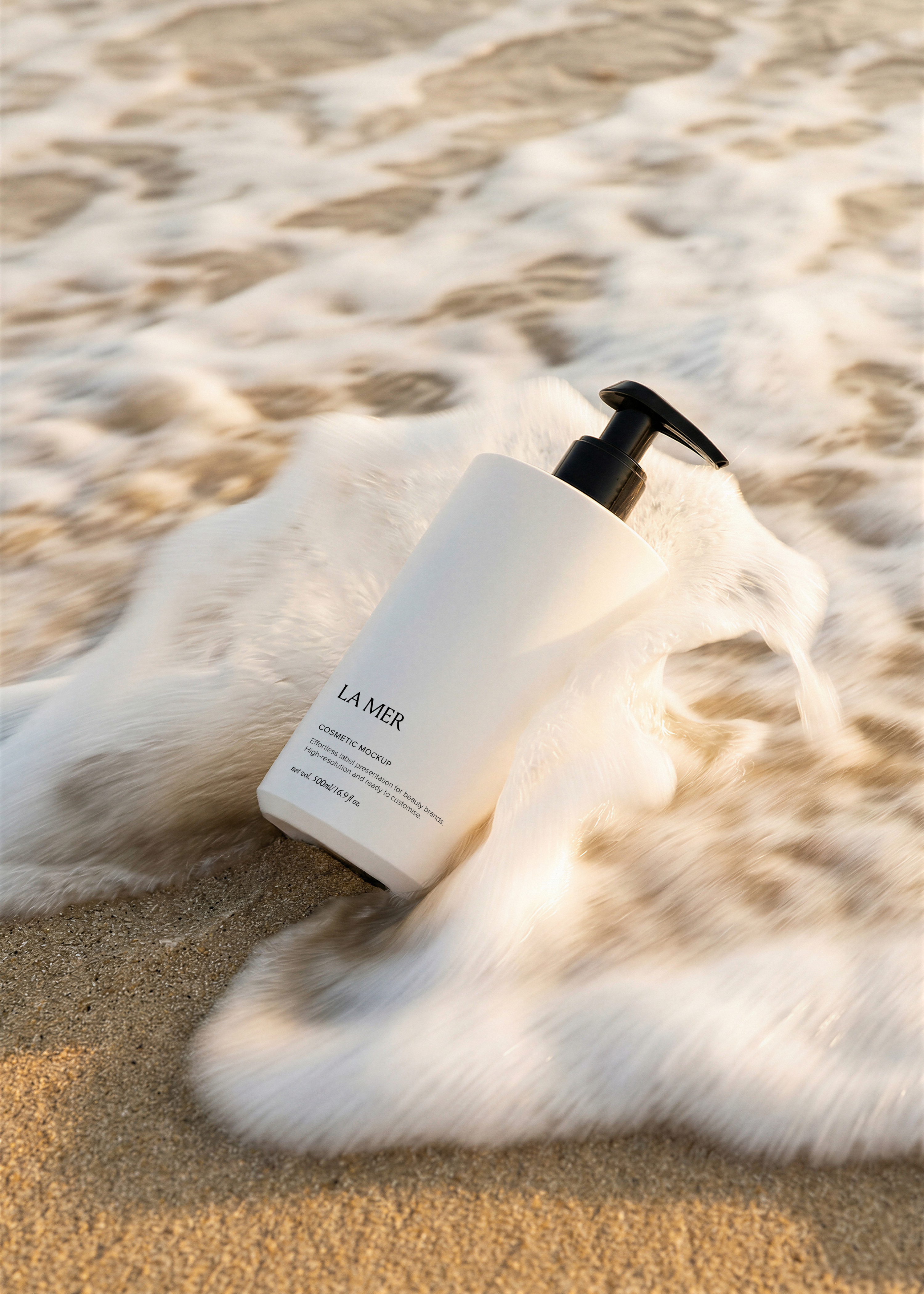White flat pump bottle with branded cosmetic label tilted in wet sand surrounded by a foamy breaking wave in golden light, from Studio Blanche