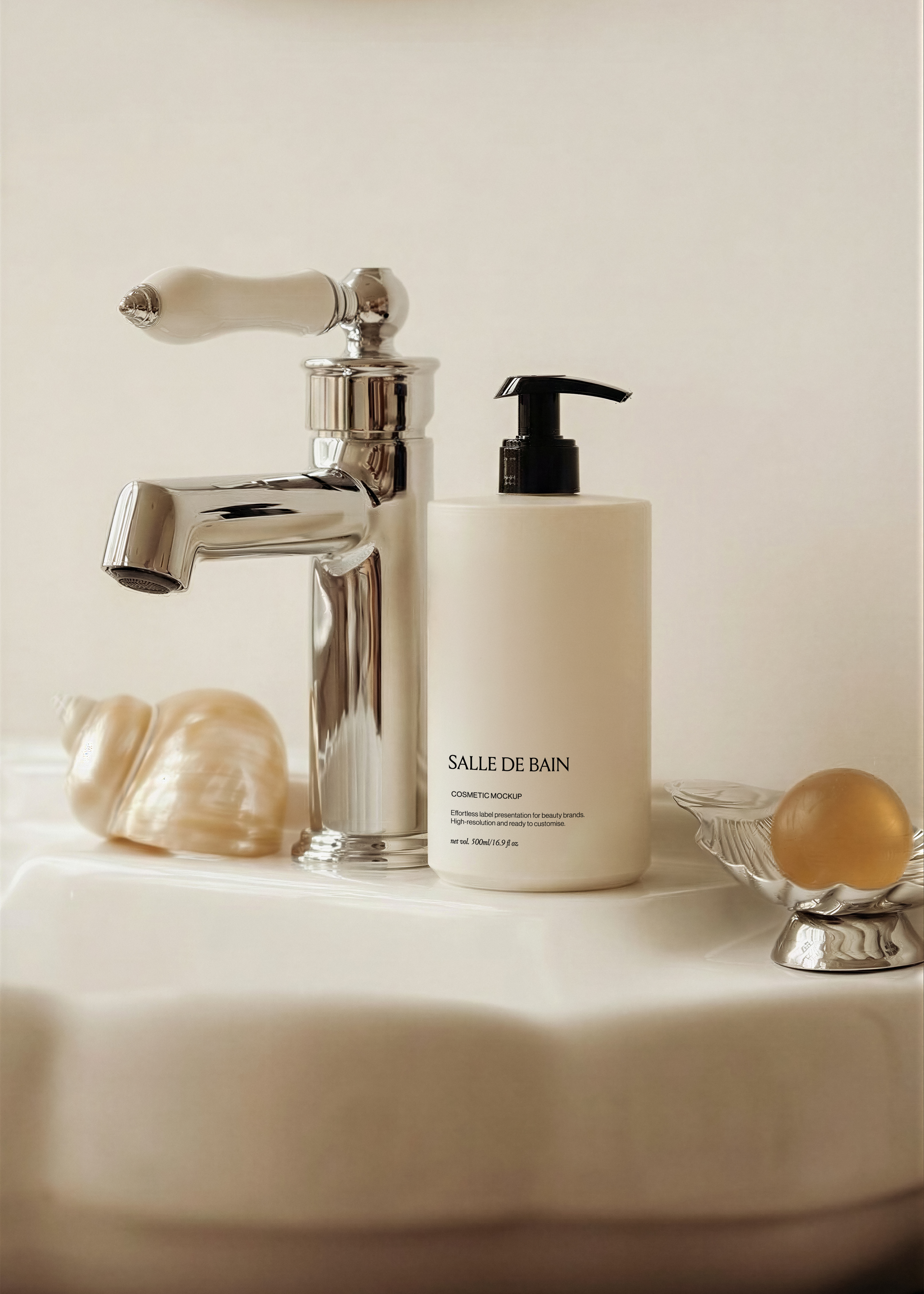 Cream cosmetic pump bottle standing on a white basin beside a chrome tap, seashell and pearl soap dish in warm light