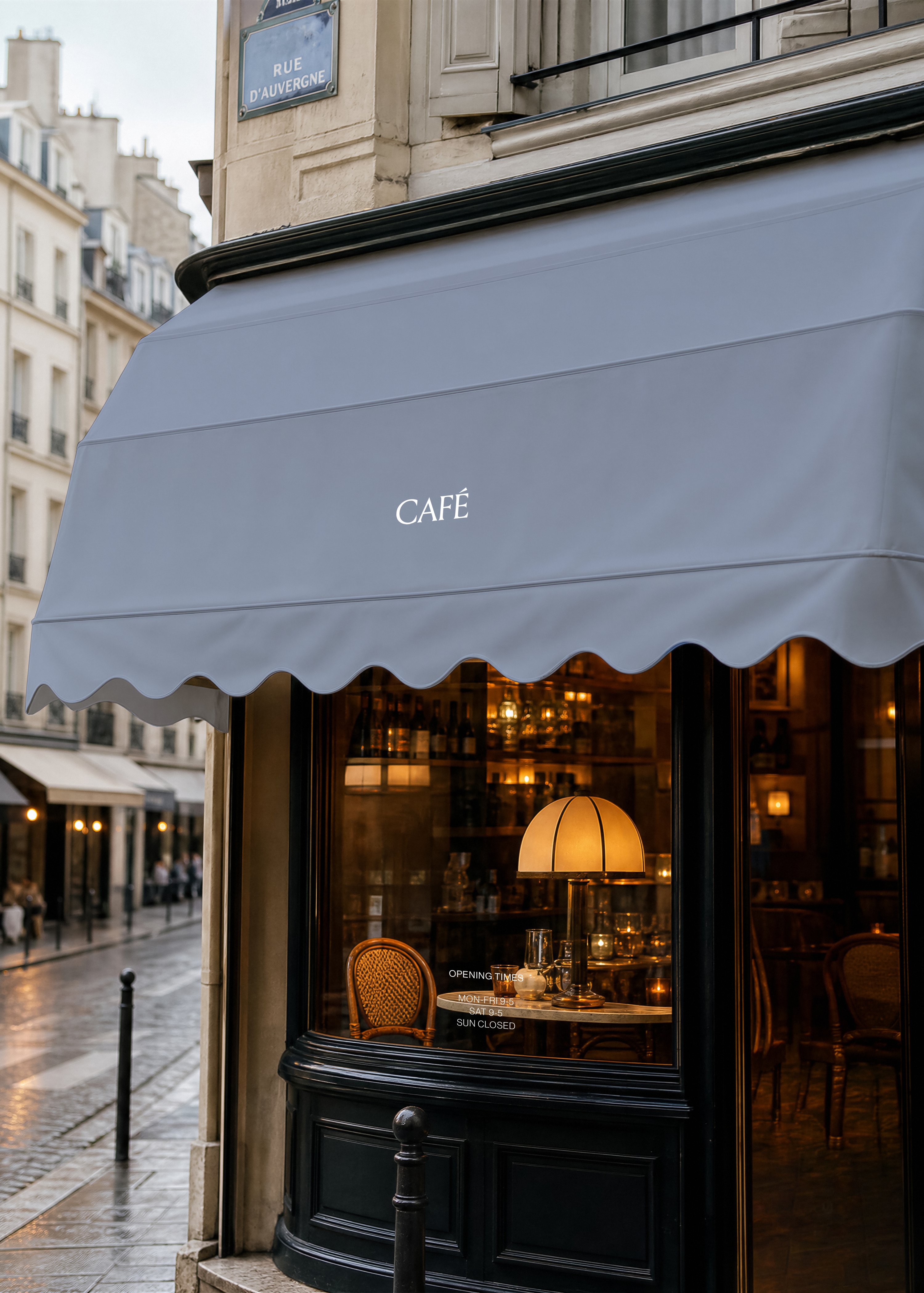 Café canopy mockup, blue-grey scalloped awning with white CAFÉ text above lit window on wet Parisian cobbled street