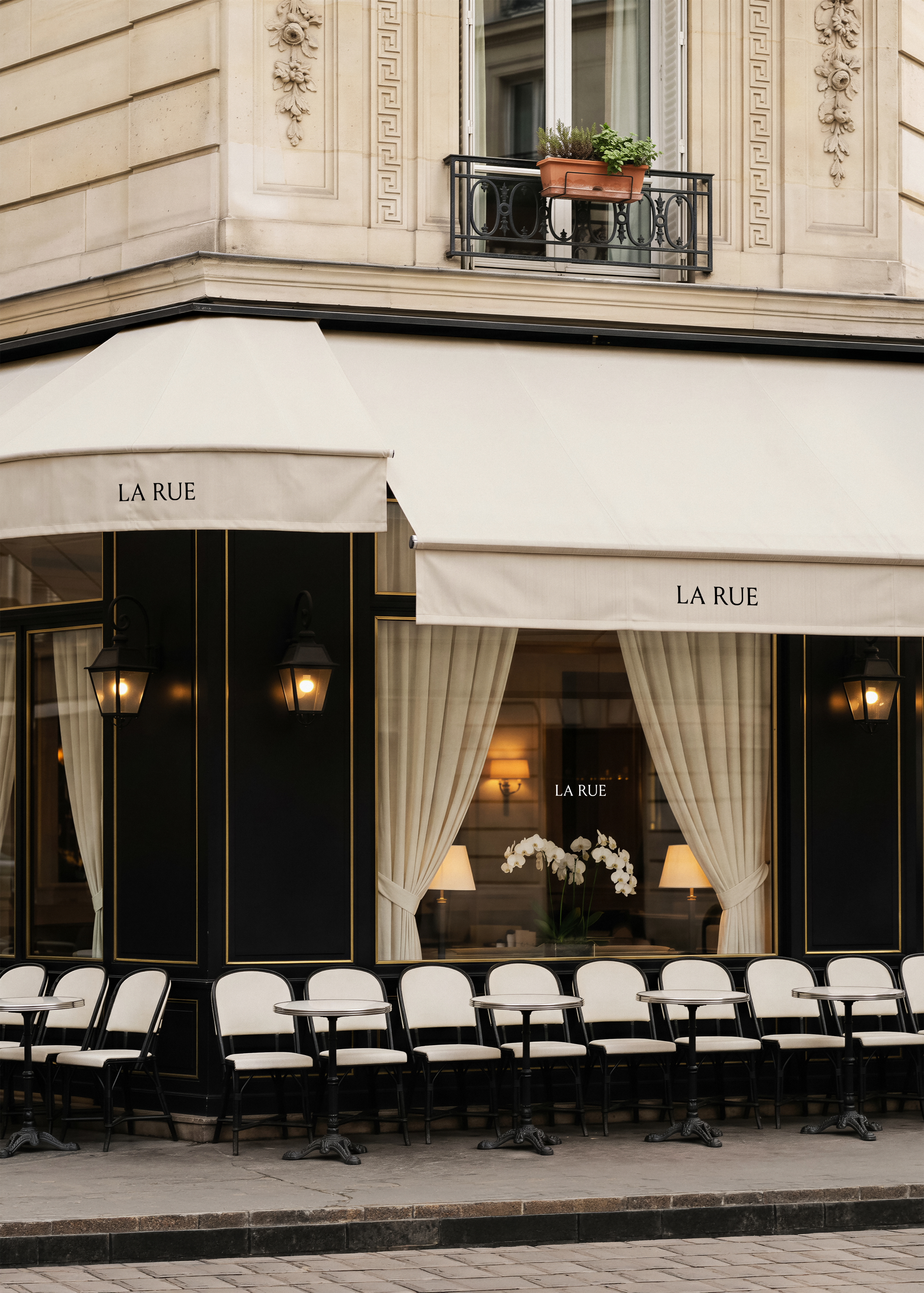 Shopfront mockup on Parisian café facade, cream canvas awning with branded lettering, black lacquered frontage, bistro chairs, stone building