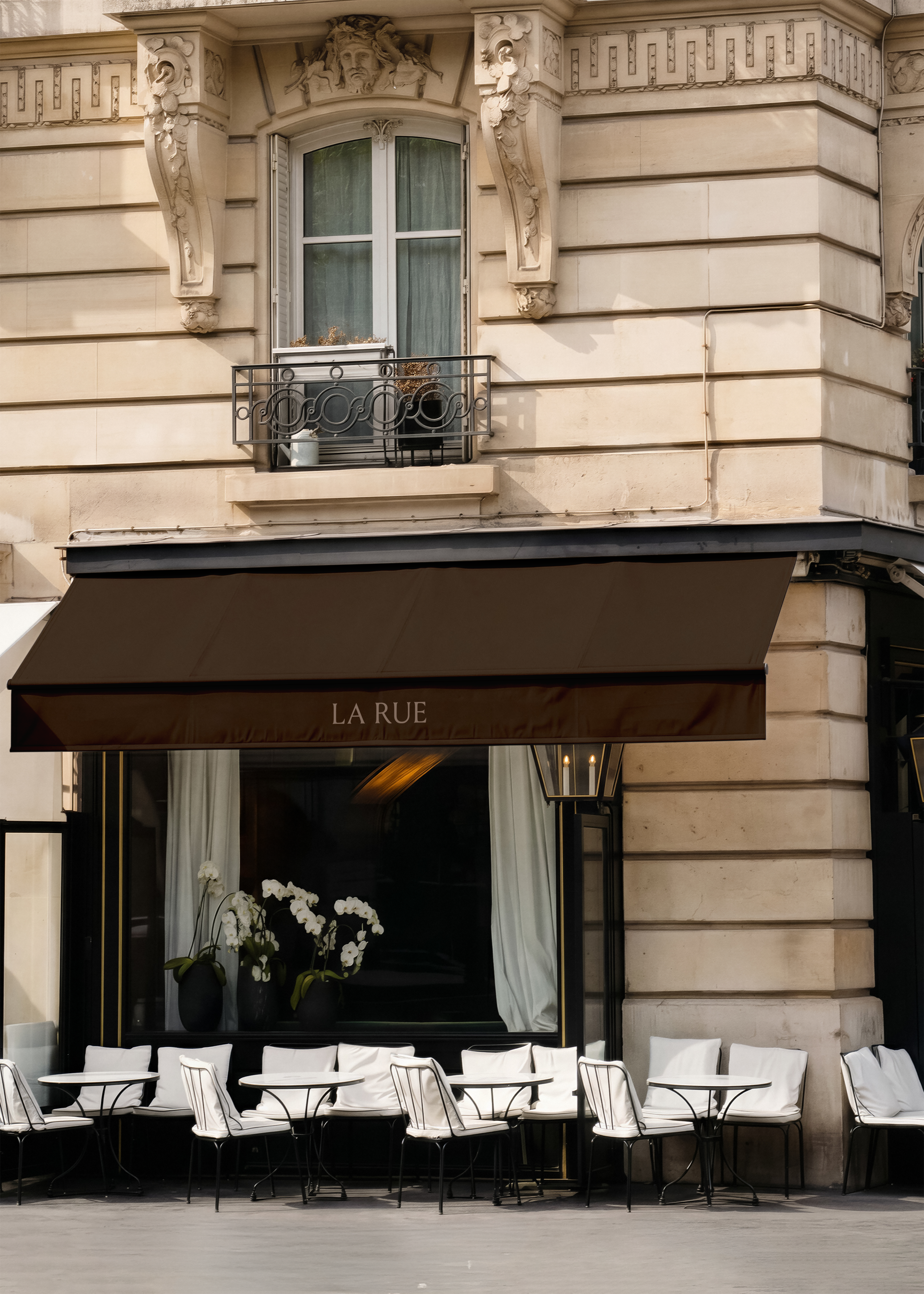 Shopfront mockup on Parisian restaurant corner, deep brown canvas awning with branded lettering, black facade, white orchids, bistro chairs