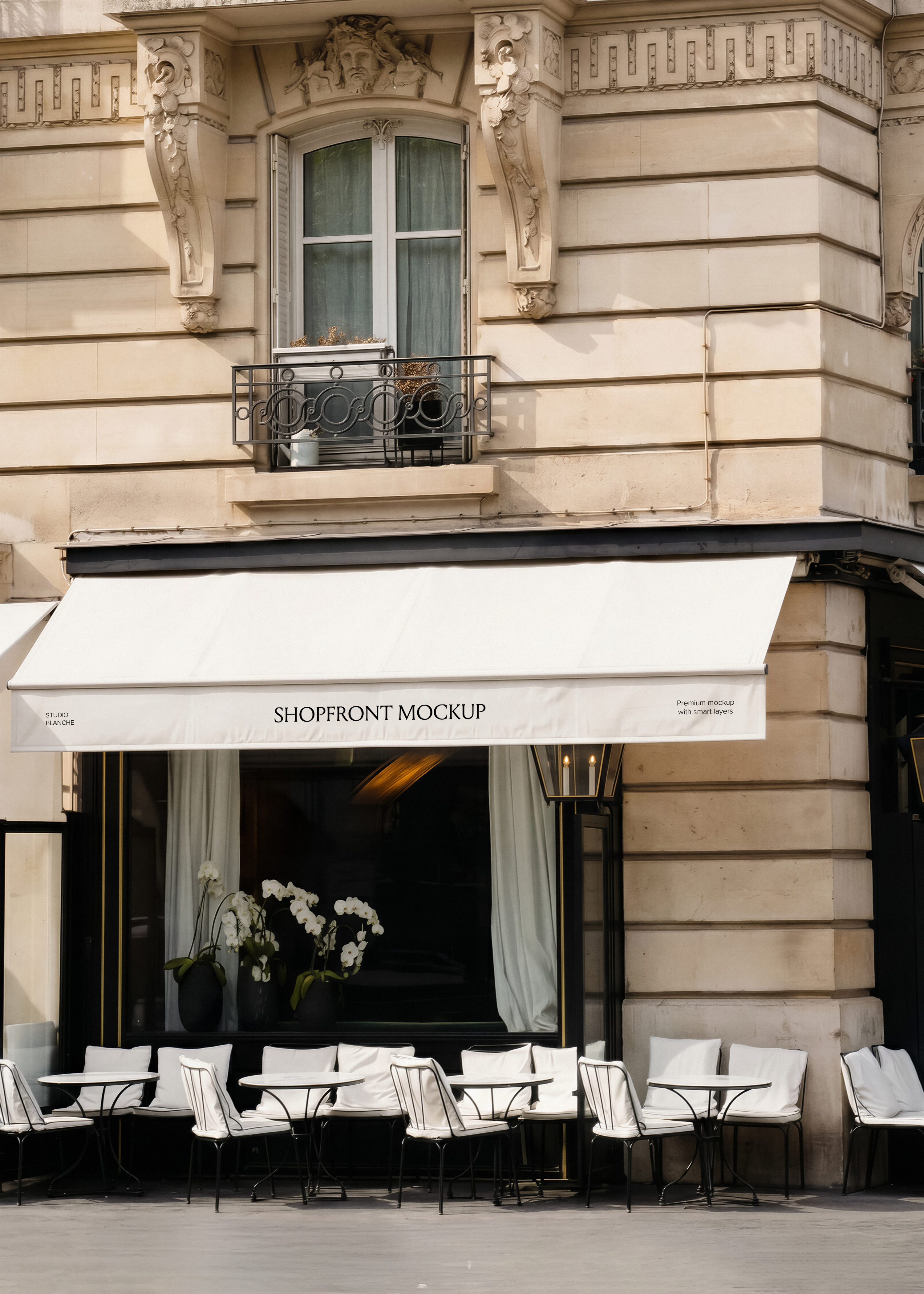 Restaurant shopfront mockup with white canvas awning, ornate Haussmann stone building, iron café chairs with white cushions, warm interior light