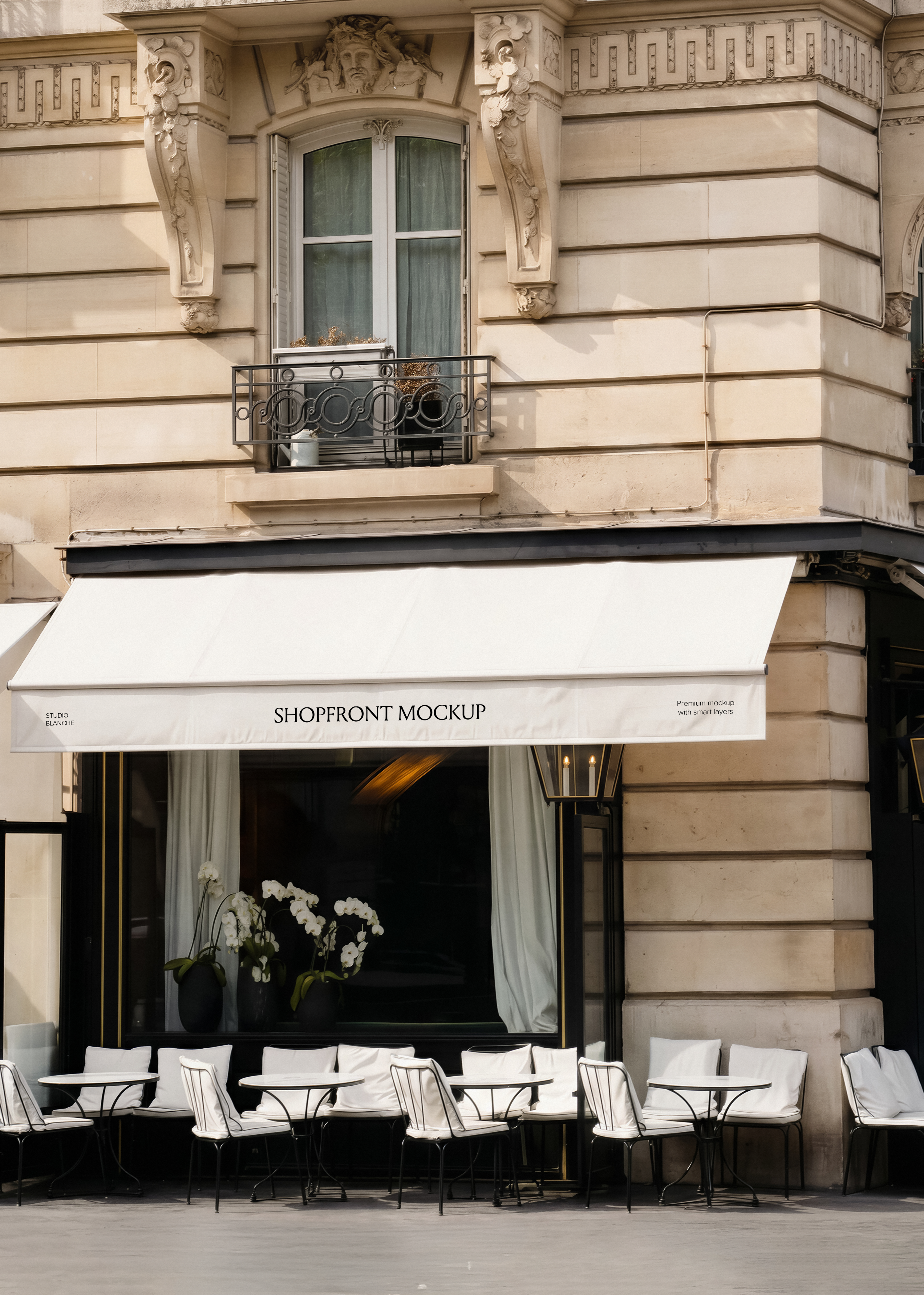 Restaurant shopfront mockup with white canvas awning, ornate Haussmann stone building, iron café chairs with white cushions, warm interior light