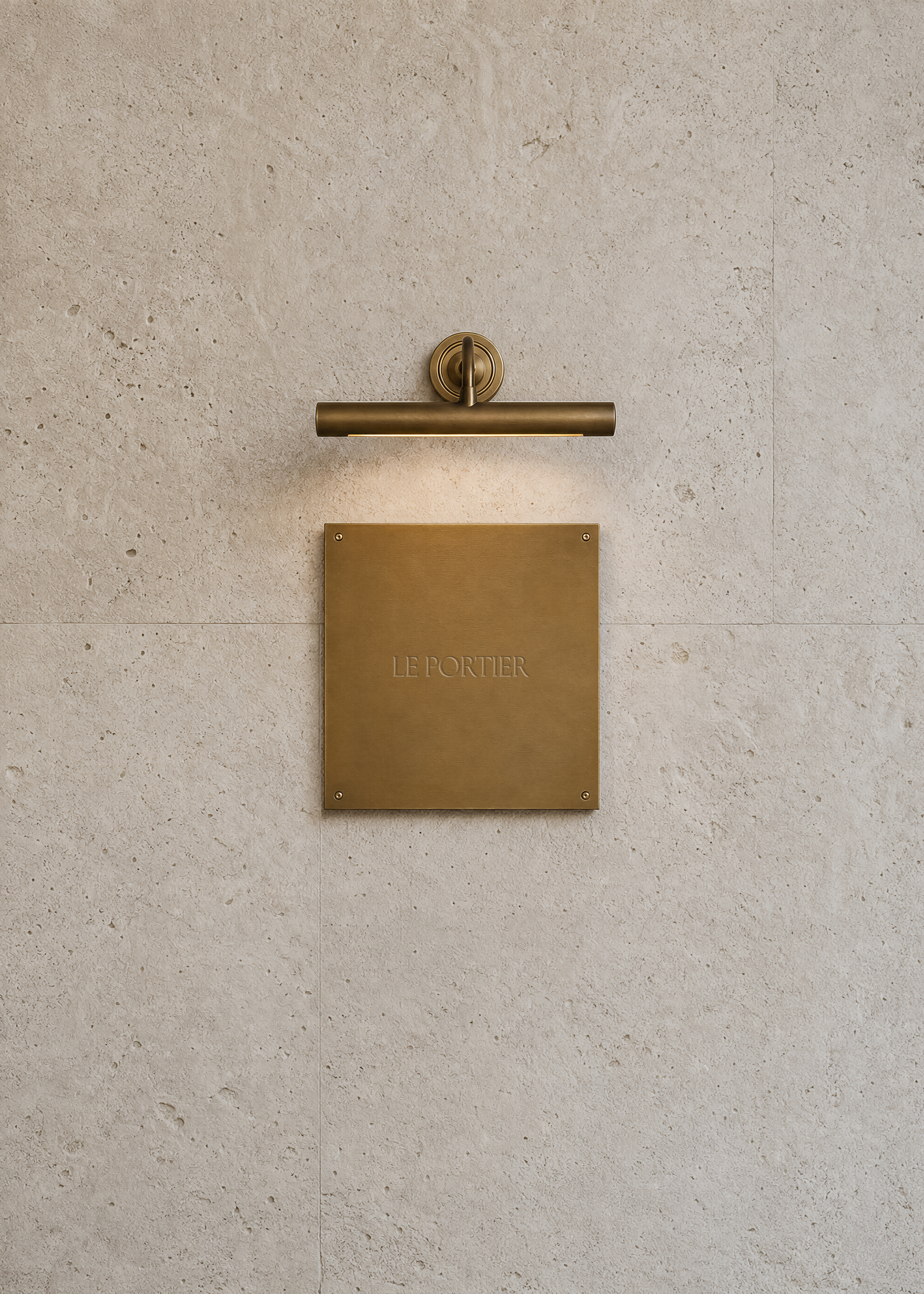 Brass sign mockup fixed to a travertine stone wall beneath a brass picture light casting a soft glow