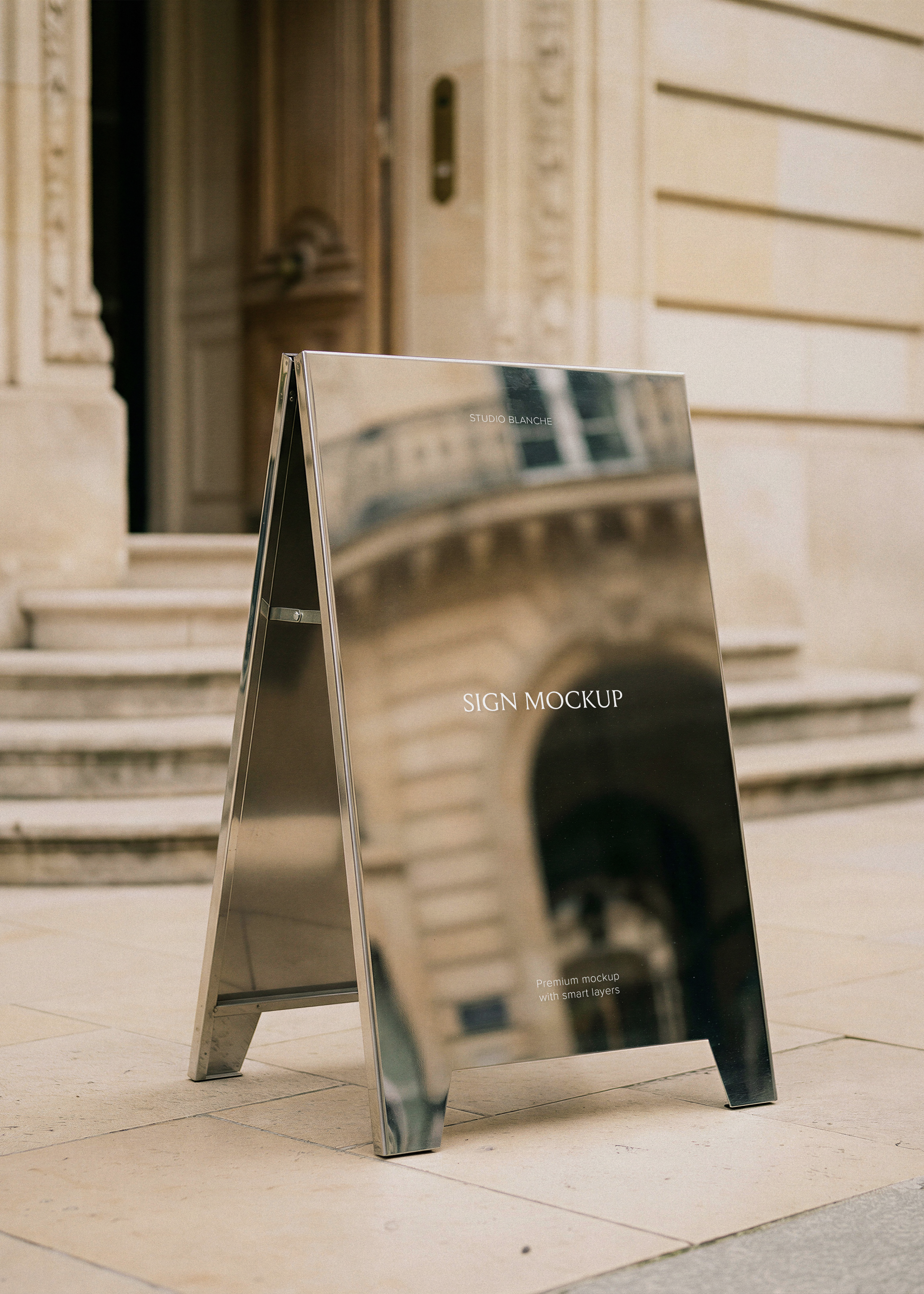 Mirror-finish steel A-frame sign mockup on stone pavement reflecting Haussmann building facade and arched doorway