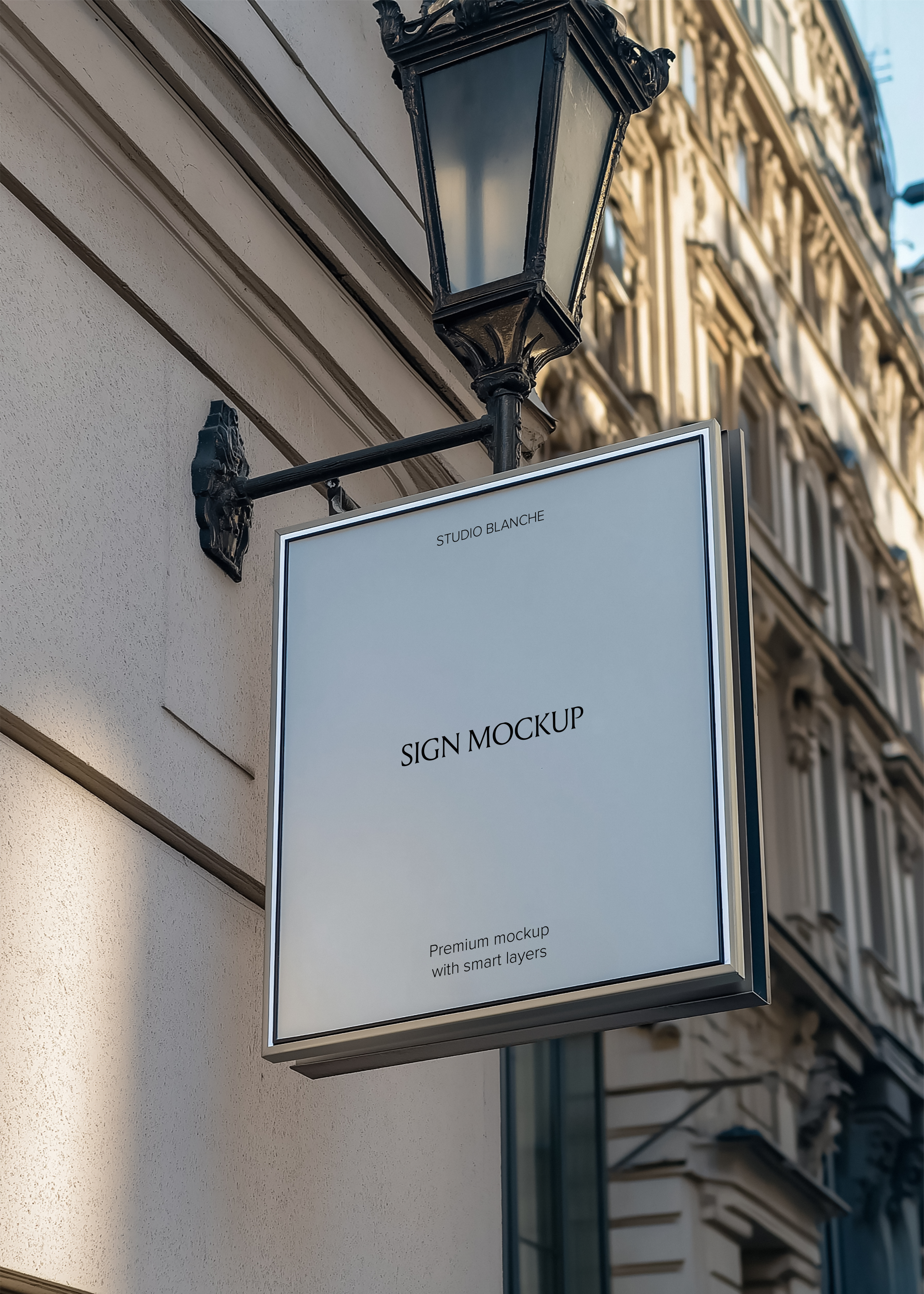 Square hanging sign mockup mounted on cream stone building facade, cast iron wall bracket and street lamp, daylight