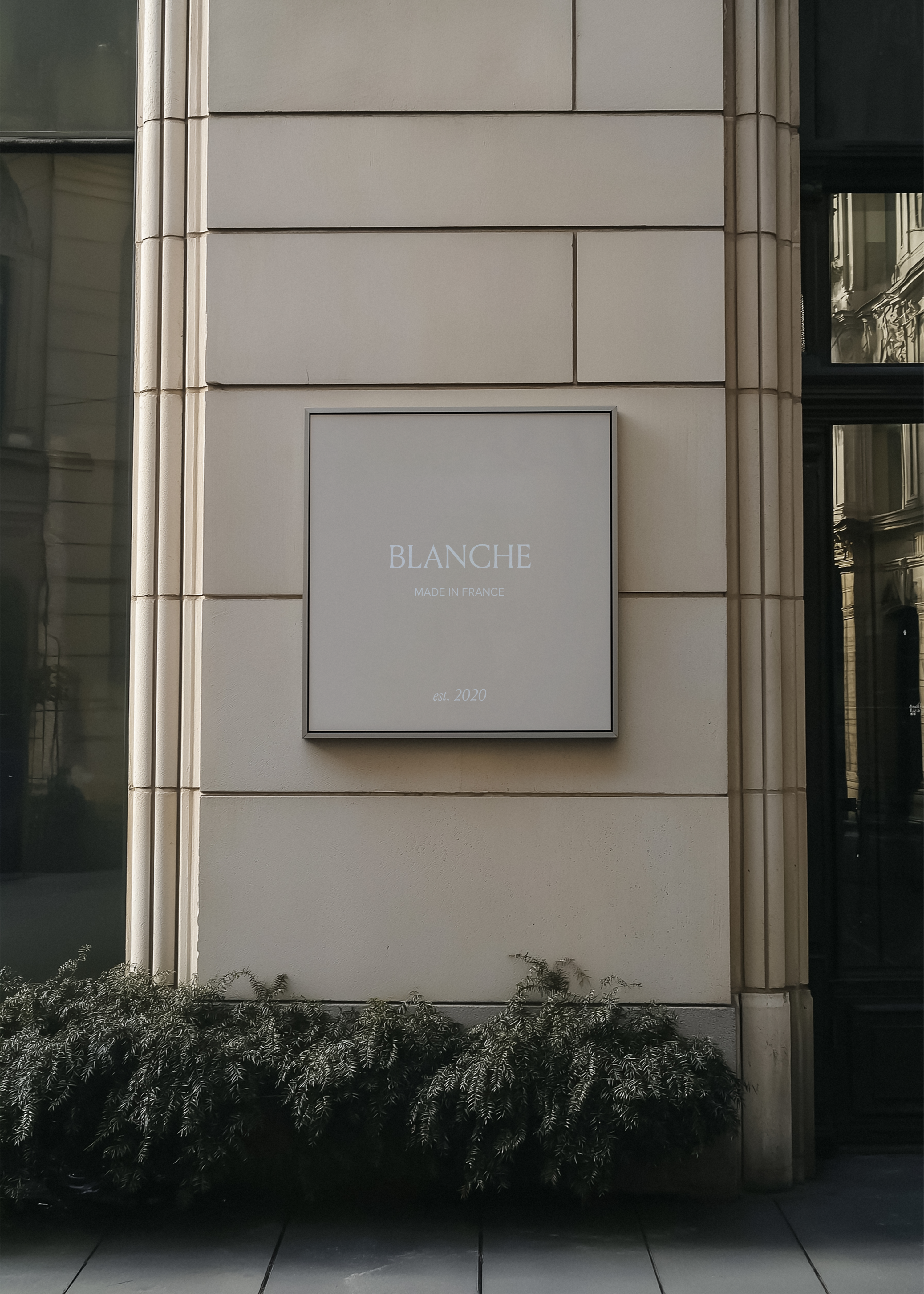 Wall sign mockup displaying white serif brand identity on grey panel, stone pillar facade and dark window frame behind