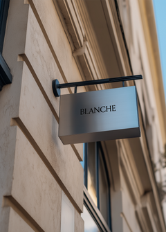 Silver metal hanging sign mockup displaying serif brand name, stone shopfront facade and tall window frame beside