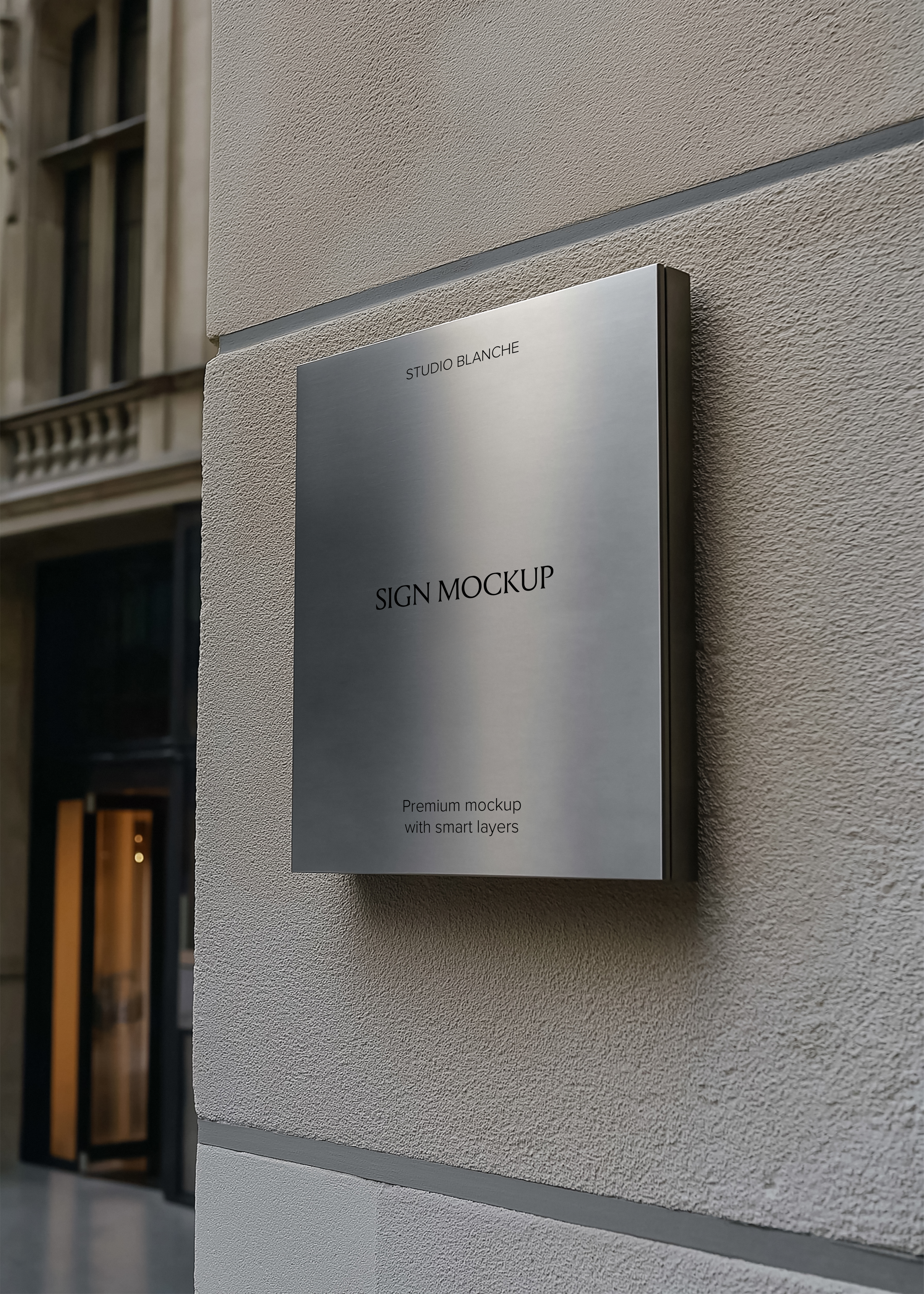 Brushed steel square sign mockup mounted on textured render wall, lit shopfront entrance visible in background, street