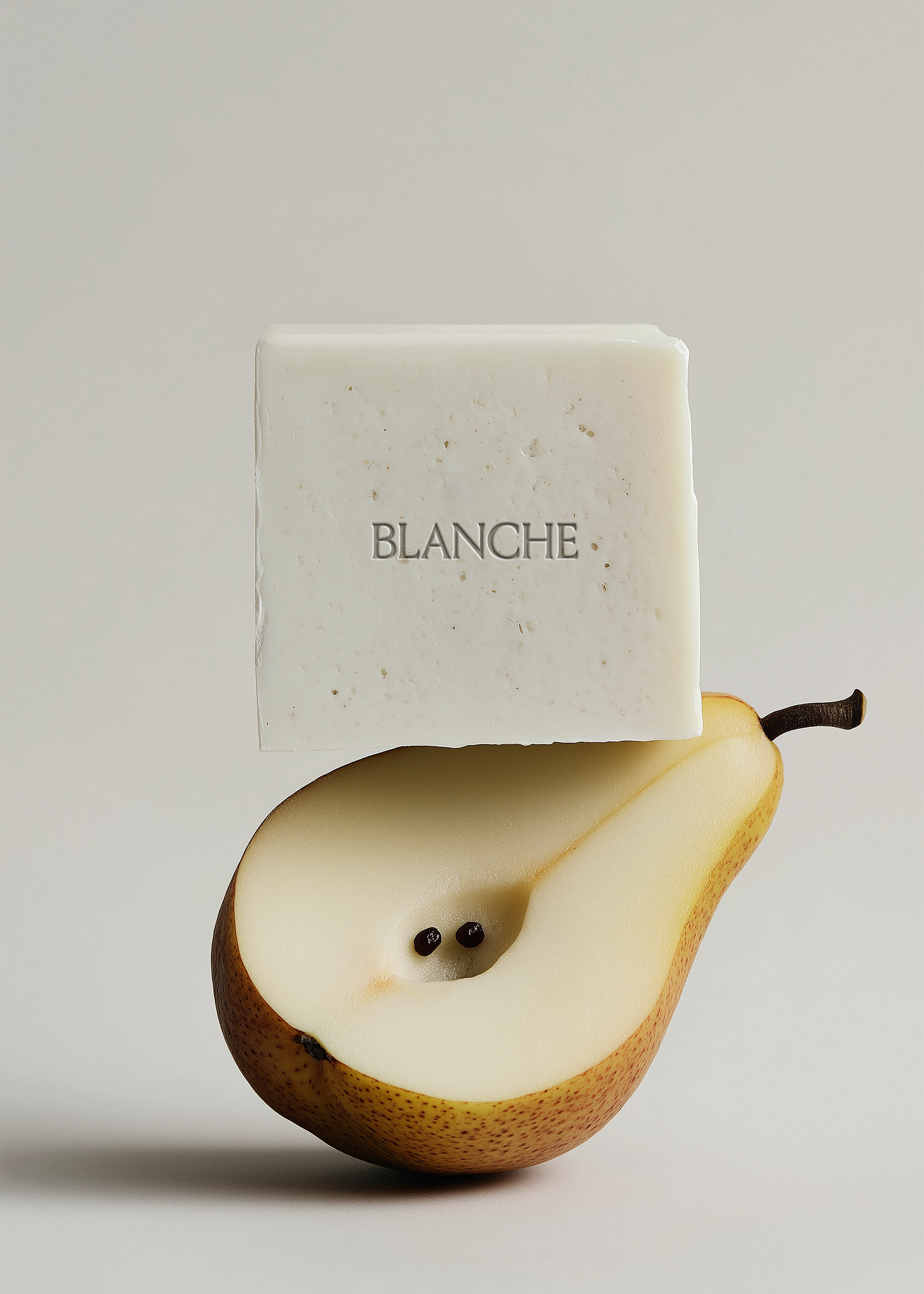 White textured soap bar balanced on halved pear, grey background, embossed brand label, natural editorial styling
