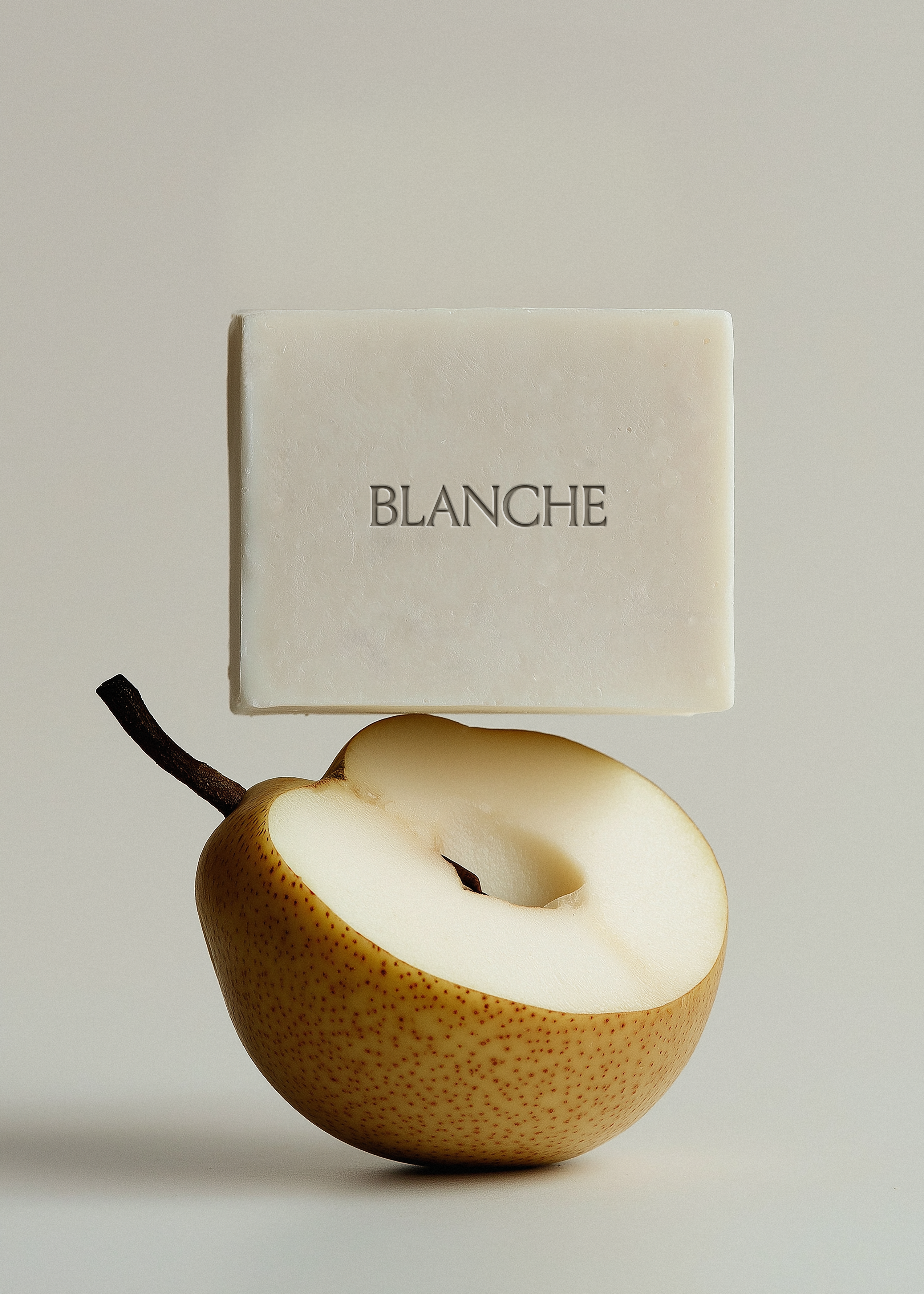 Cream rectangular soap bar balanced on halved nashi pear, grey background, embossed brand label, editorial styling