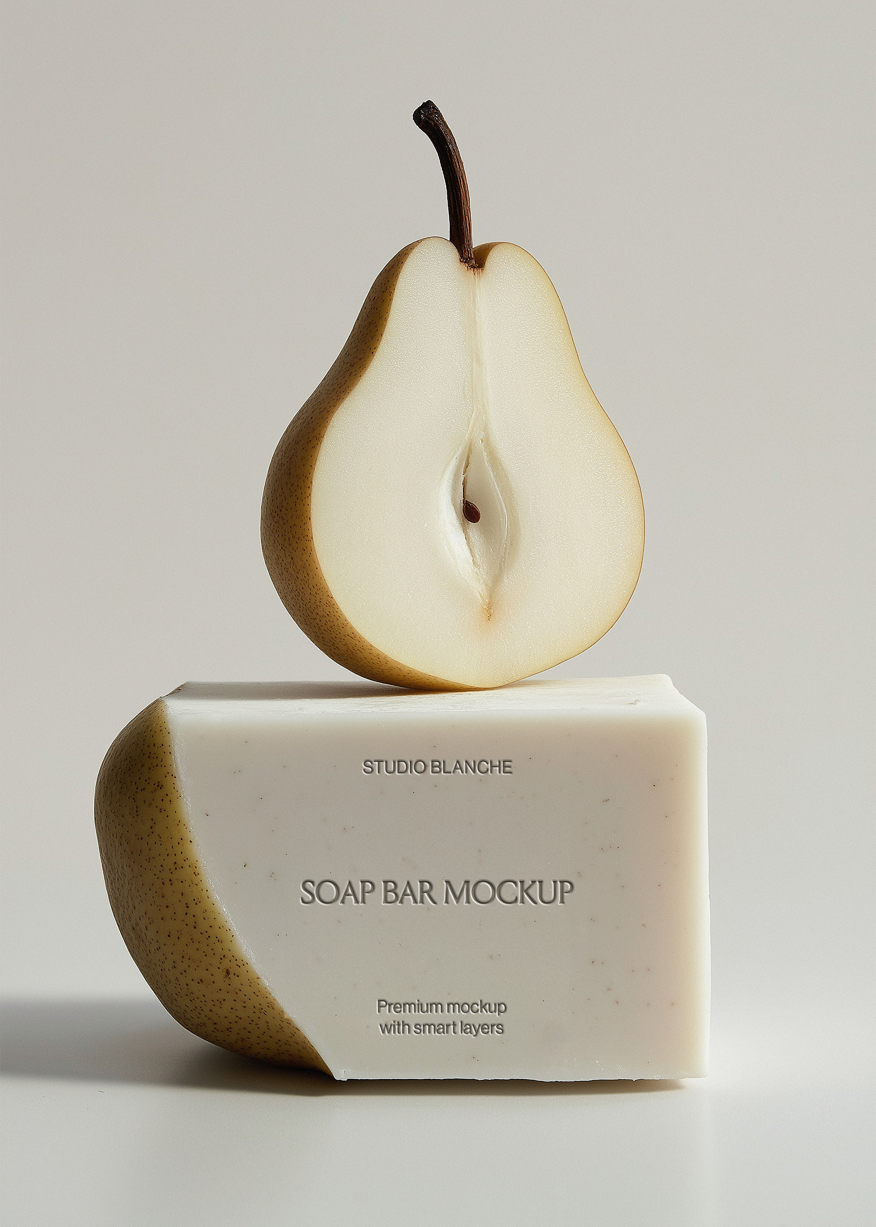 Chunky white soap bar mockup with sliced pear resting on top, Studio Blanche label placeholder, grey backdrop