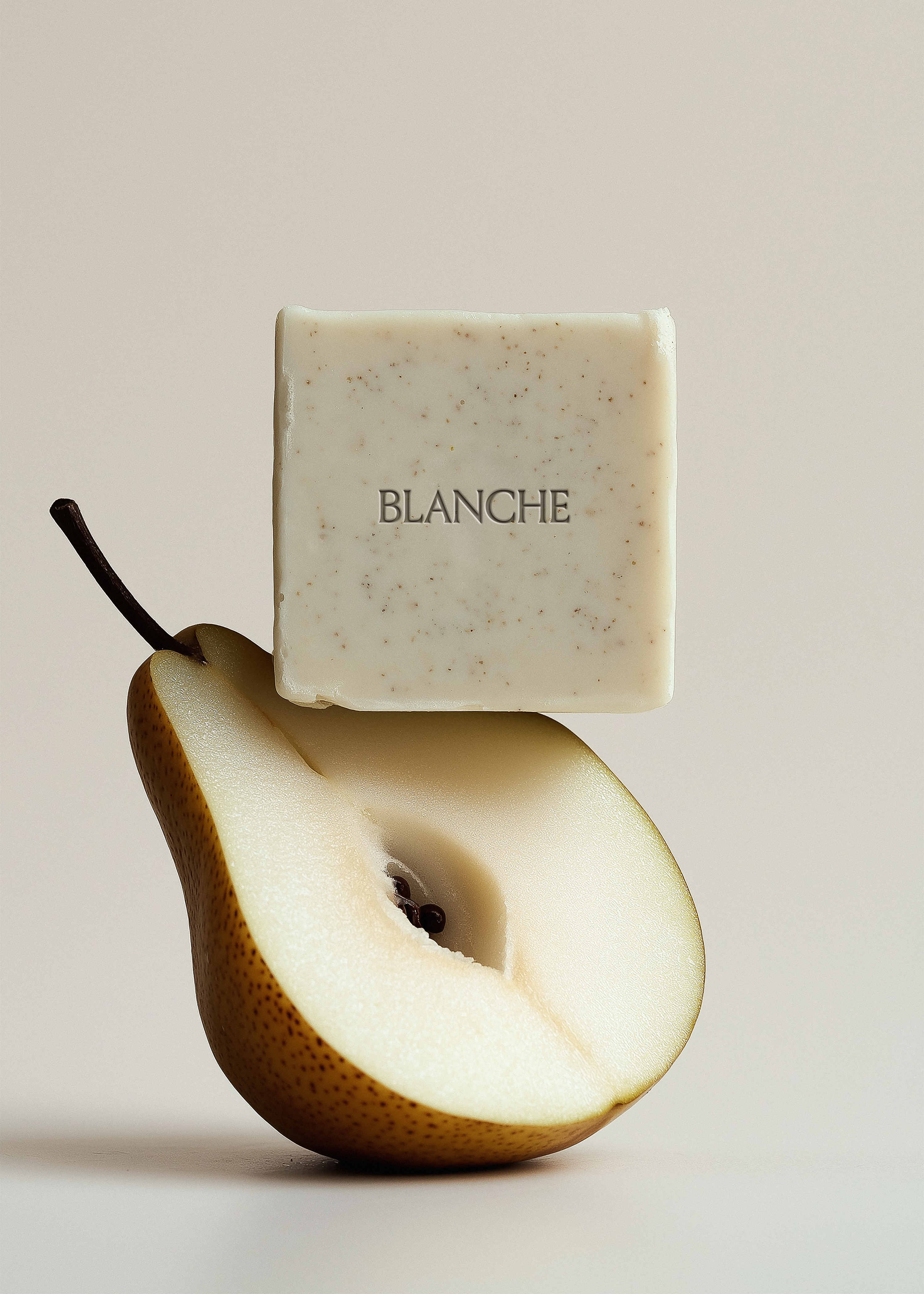 Speckled white square soap bar balanced on halved pear, warm stone background, embossed brand label, editorial styling