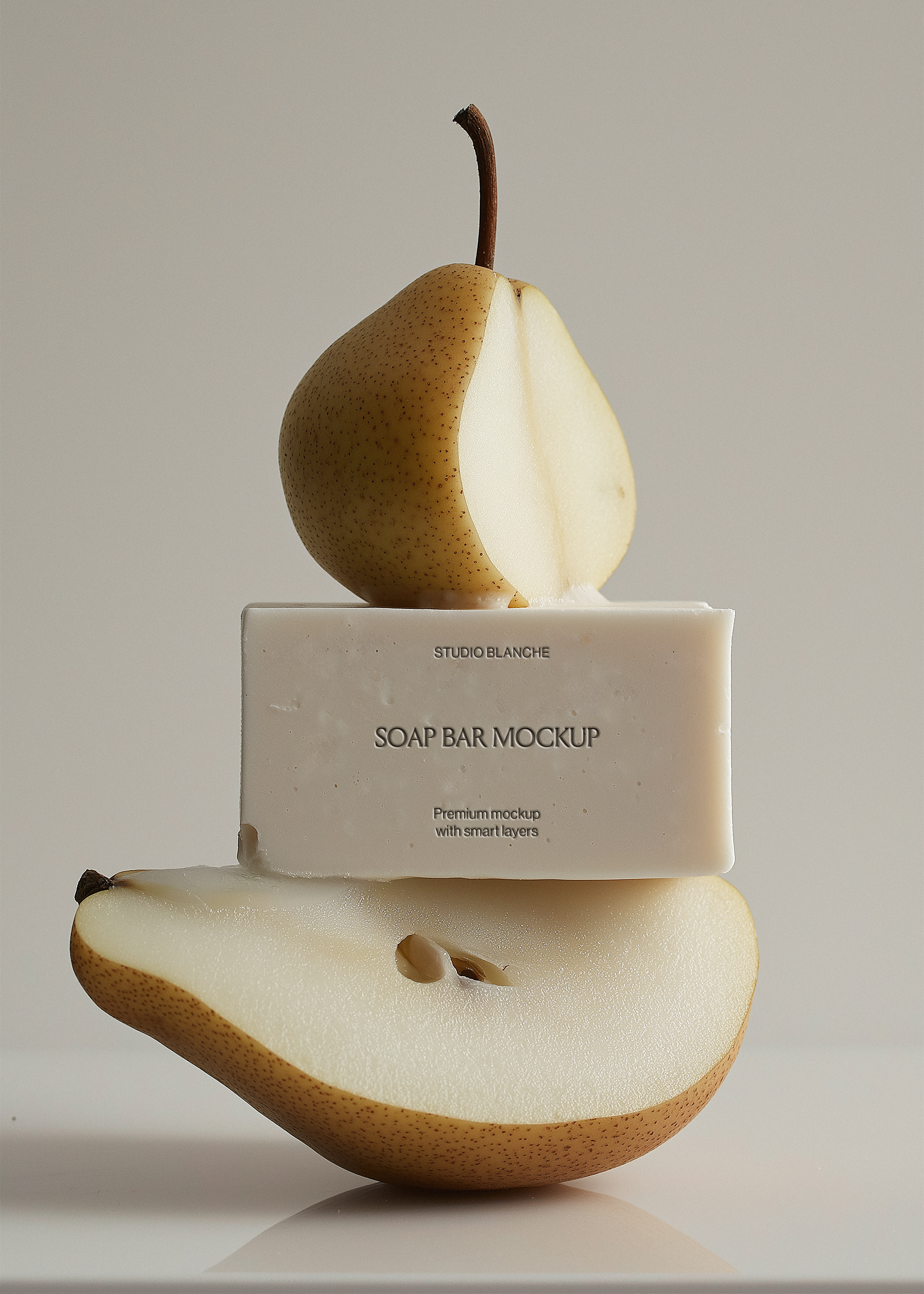 Landscape soap bar mockup between sliced pears, reflective surface, Studio Blanche label placeholder, soft grey backdrop