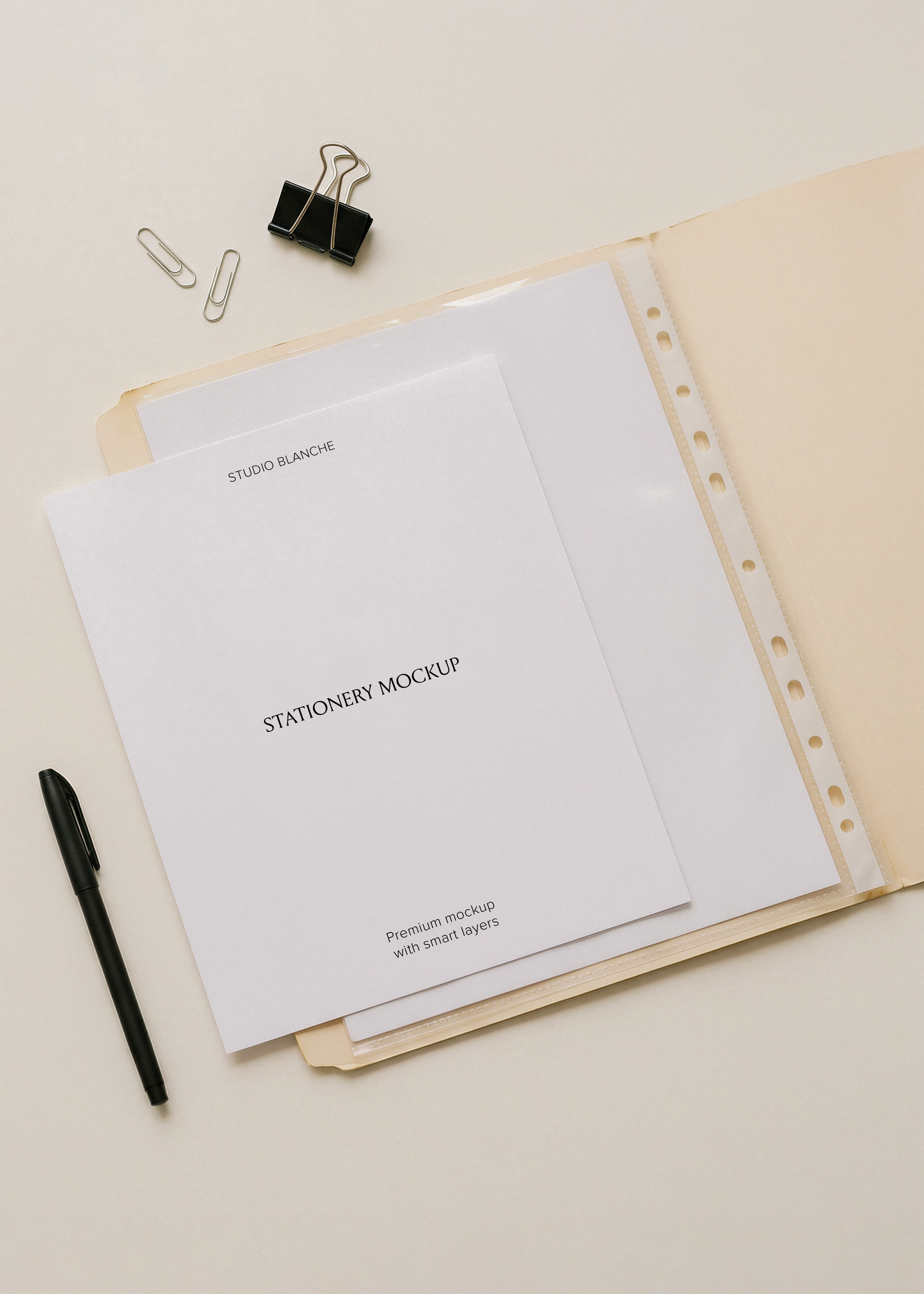 Blank A4 letterhead on cream archival folder with punched pocket, black pen and silver paper clips, minimal flat lay