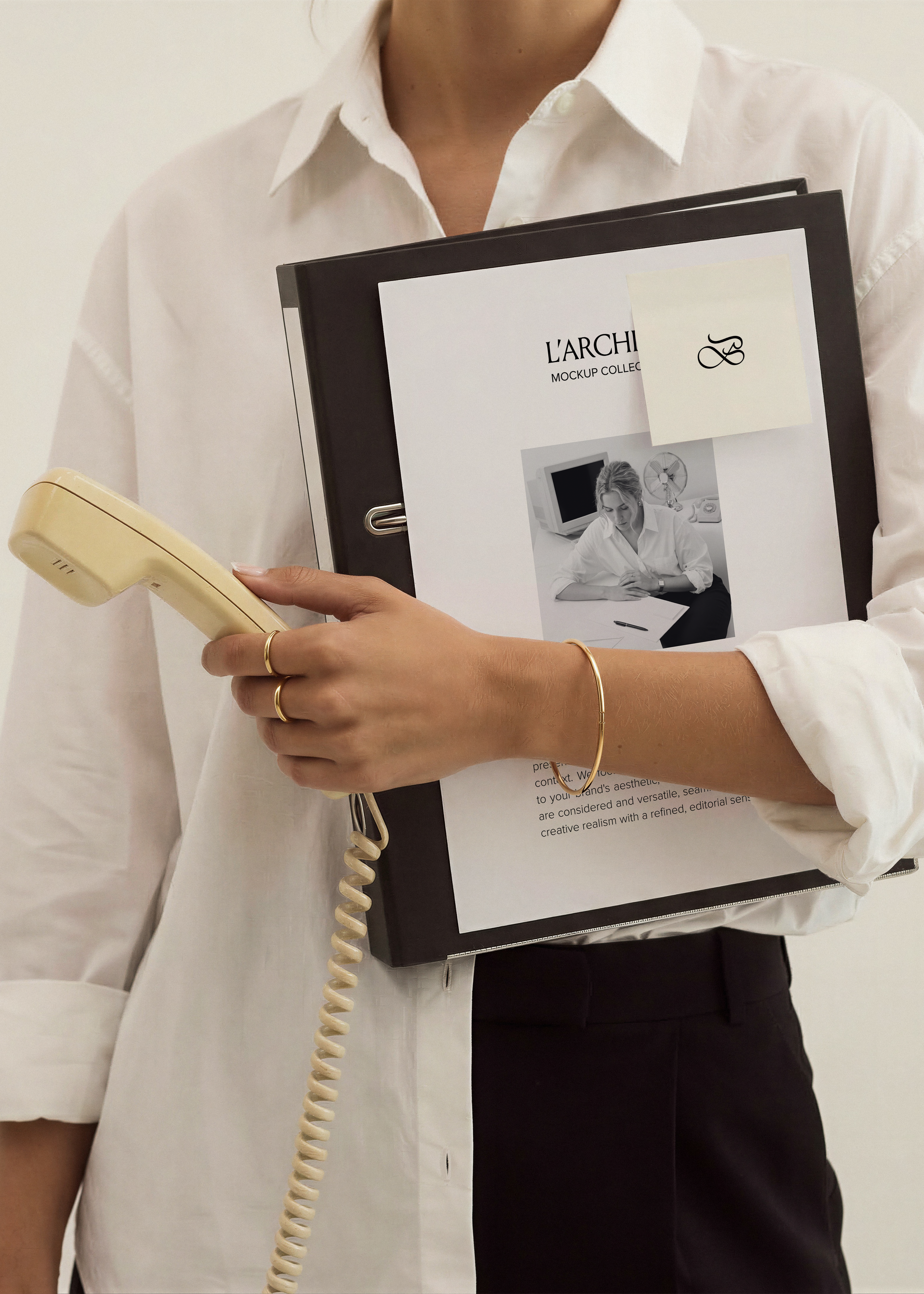 A4 card and sticky note stationery mockup held against black binder with white shirt, gold bangle and cream rotary handset