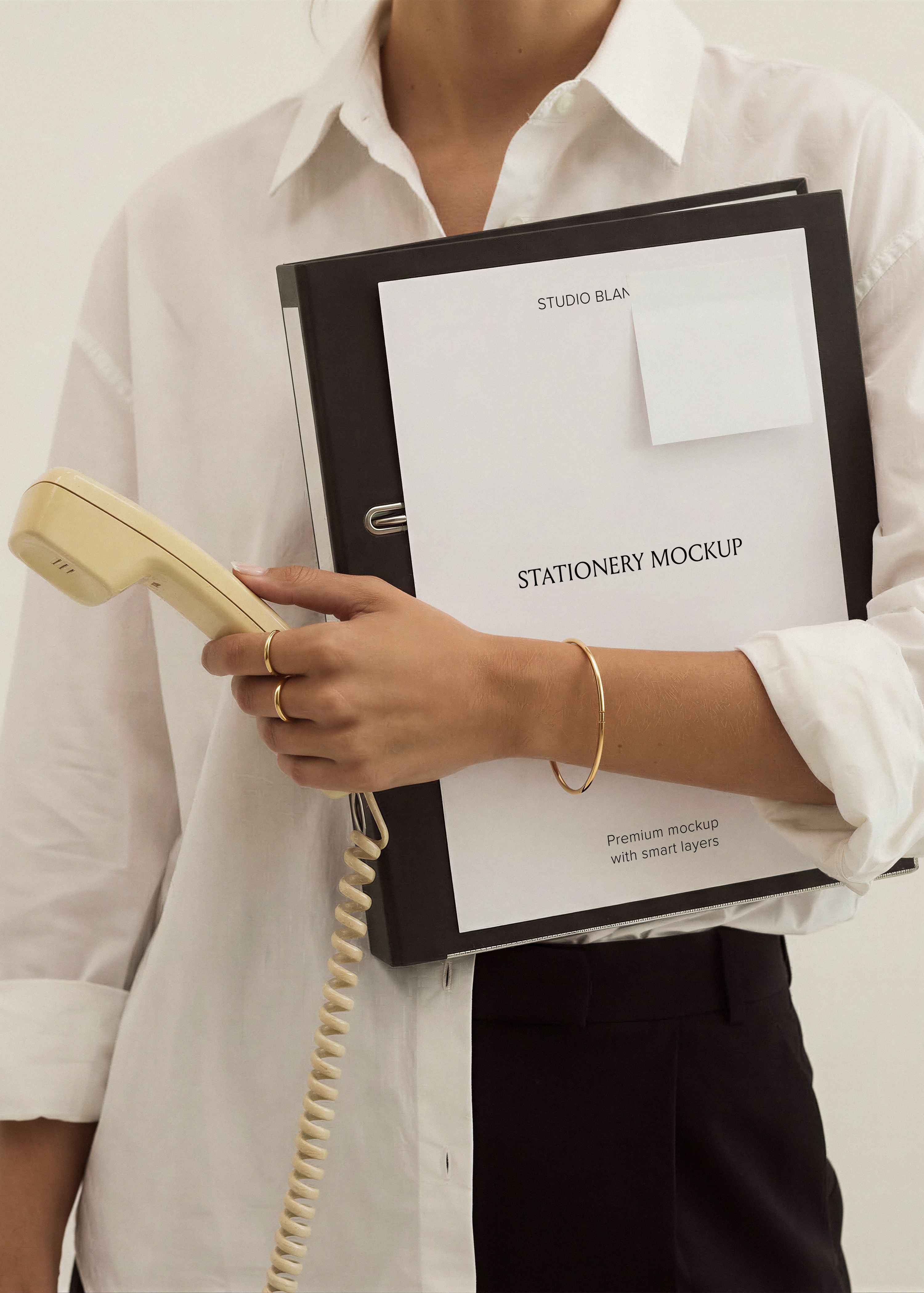 Blank A4 card with small sticky note pinned to black leather folder, cream vintage phone handset and coiled cord visible