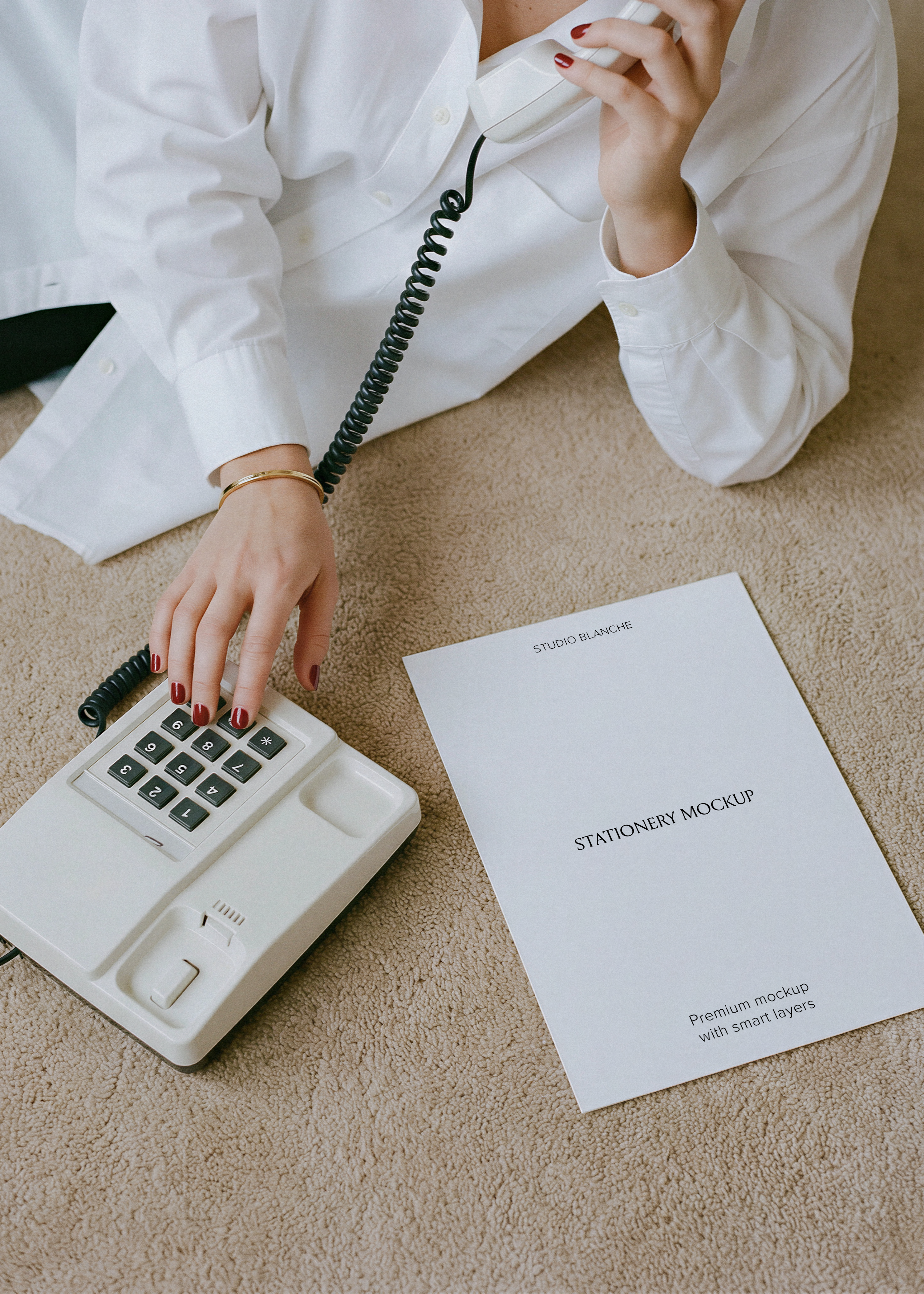 Blank A4 letterhead laid on carpet next to cream vintage telephone, white shirt sleeve and coiled cord, editorial scene