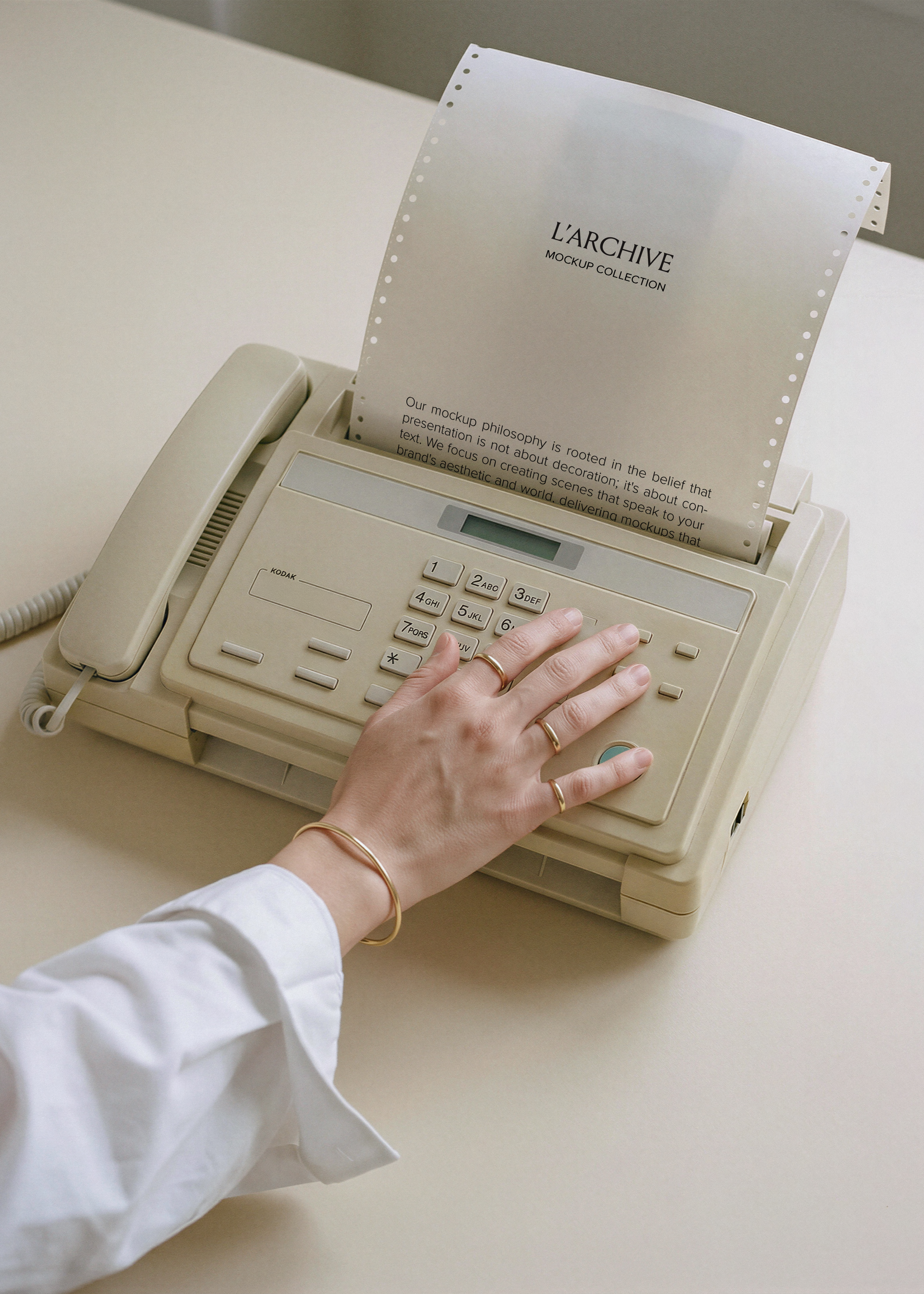 Continuous feed paper stationery mockup emerging from cream vintage fax machine, hand resting on keypad with gold rings