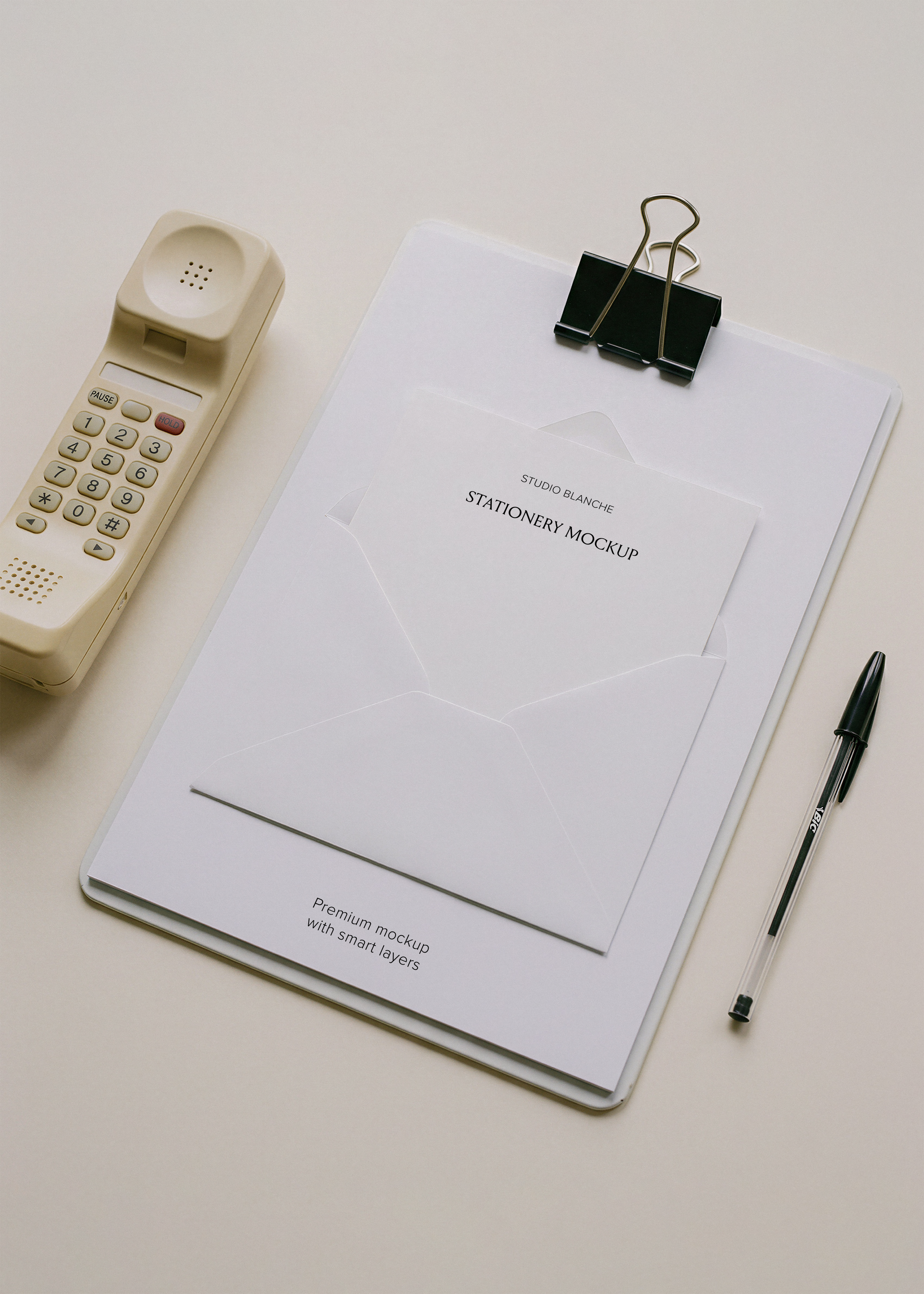 Blank A4 letterhead and white envelope on clipboard beside retro cordless phone and biro pen, minimal editorial desk