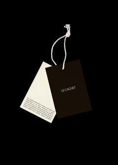 Two swing tag mockups hanging from white cotton cord on black, one dark brown with serif type, one cream
