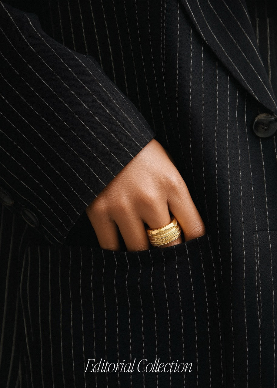Hand wearing a gold ring on a black pinstripe suit background