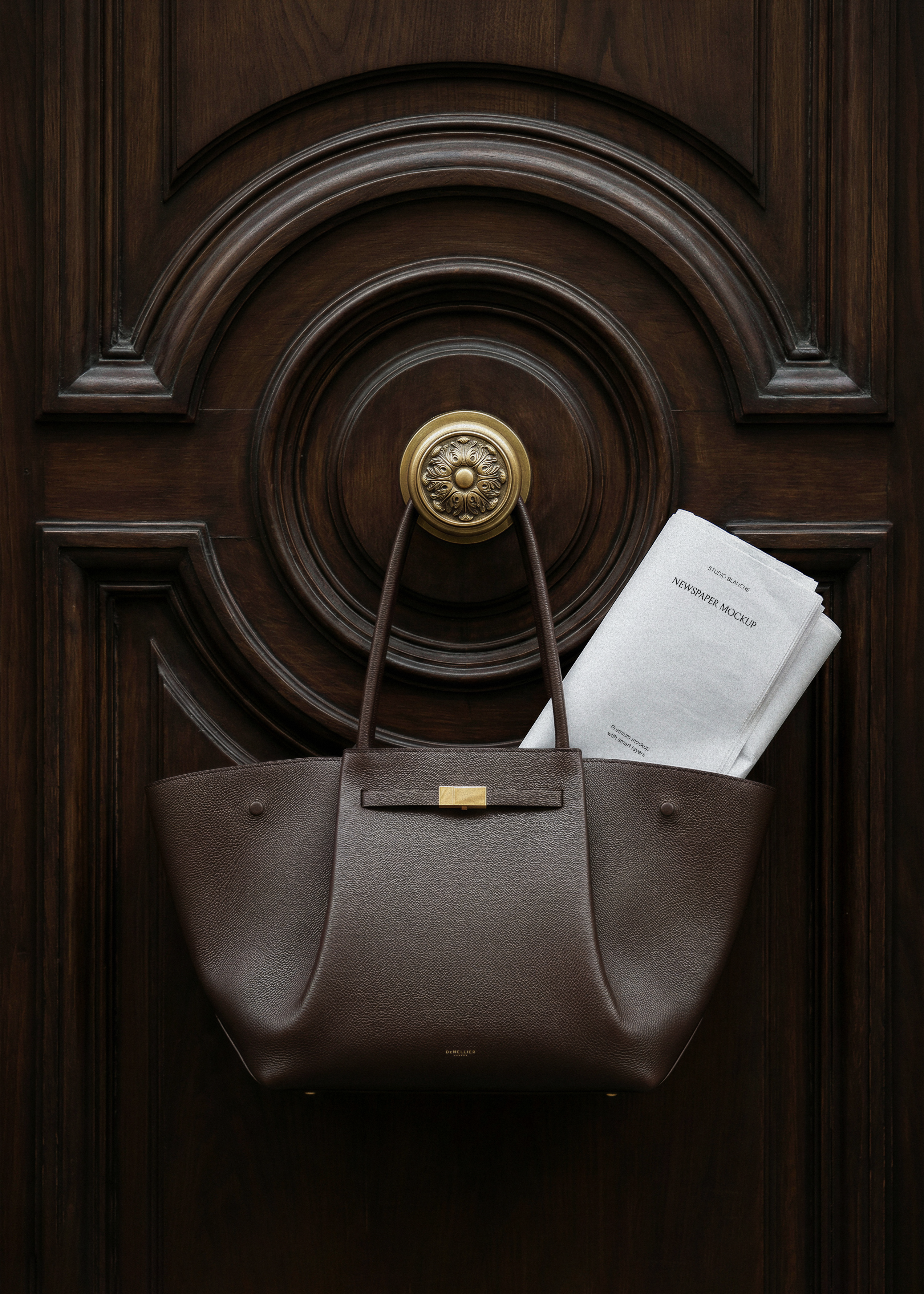 Newspaper mockup in dark leather Demellier tote bag hanging on ornate wooden door with brass knob, from Studio Blanche