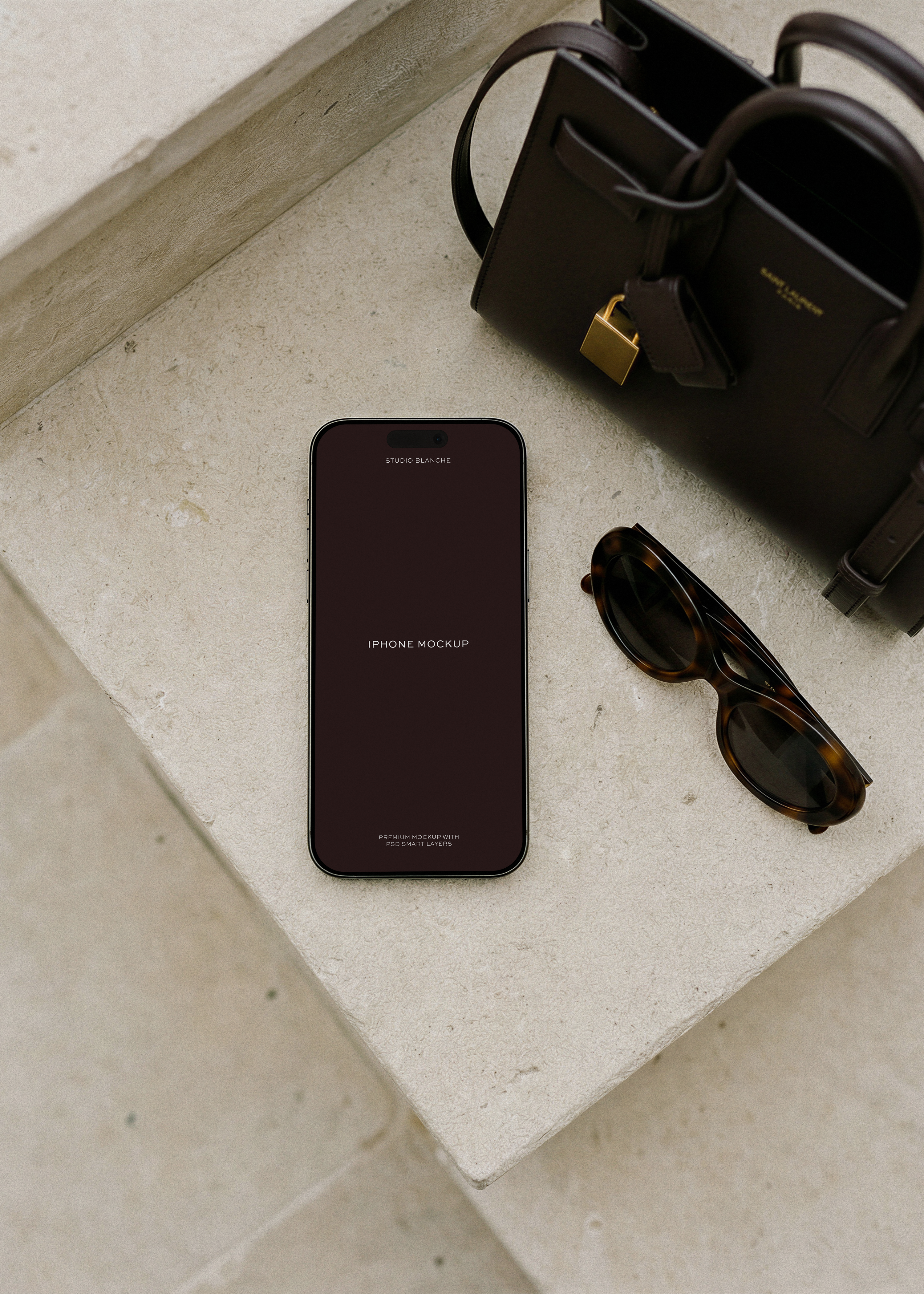 iPhone mockup on travertine with leather Saint Laurent handbag and Celine sunglasses, from Studio Blanche