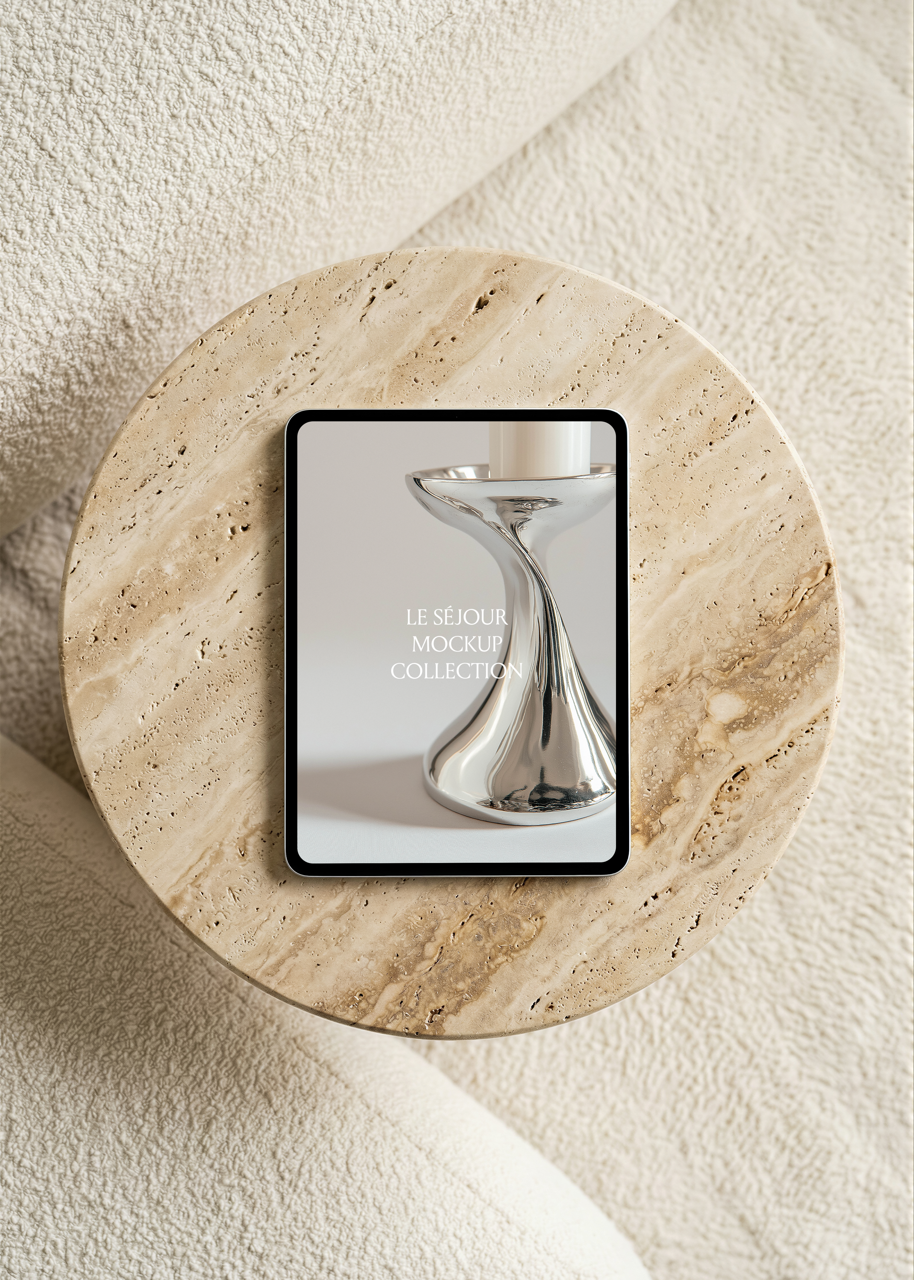 iPad mockup lying flat on a round travertine side table seen from above, surrounded by cream boucle sofa upholstery