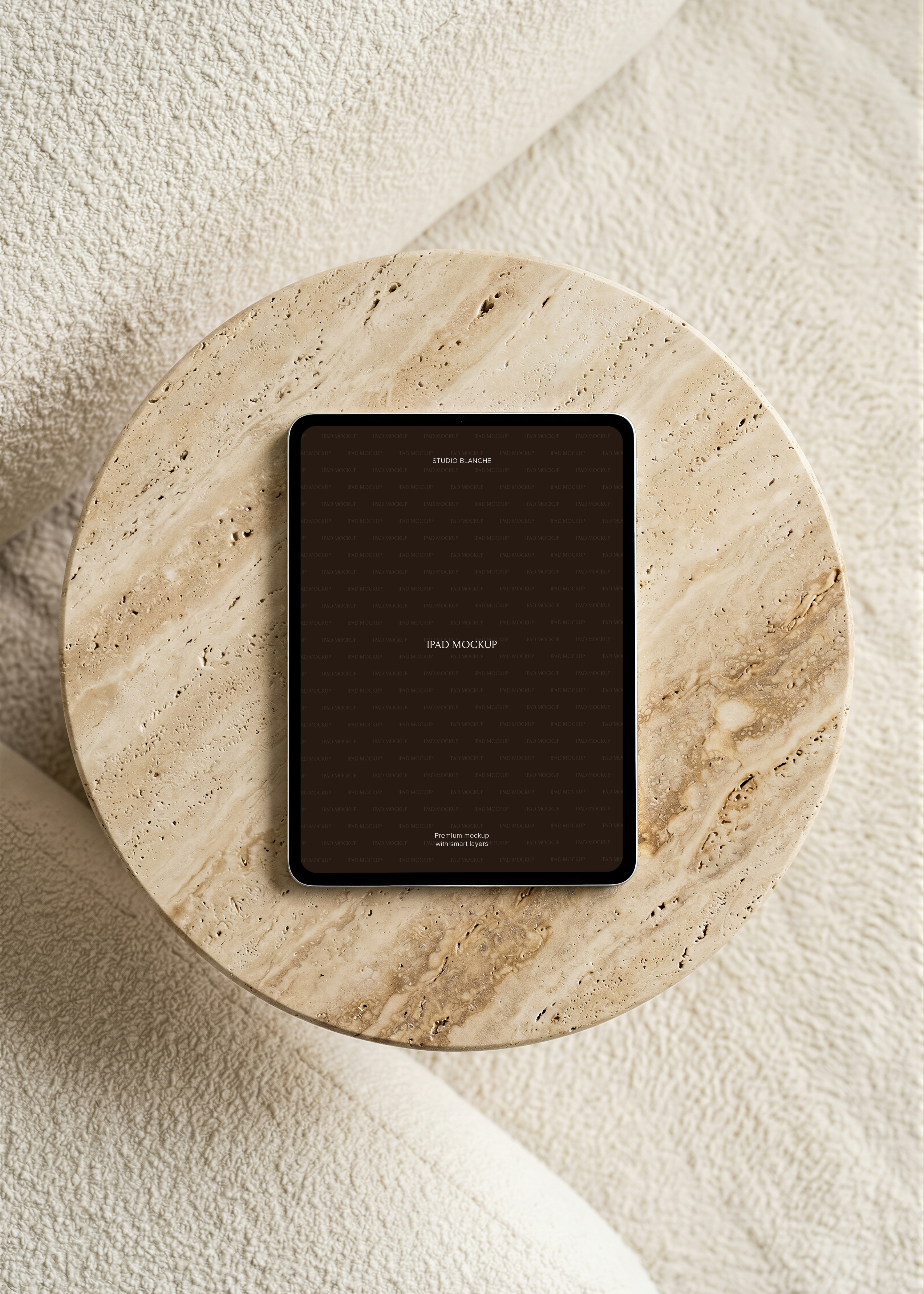 Overhead iPad mockup detail with a dark portrait screen and silver edge on porous beige travertine stone, soft neutral tones