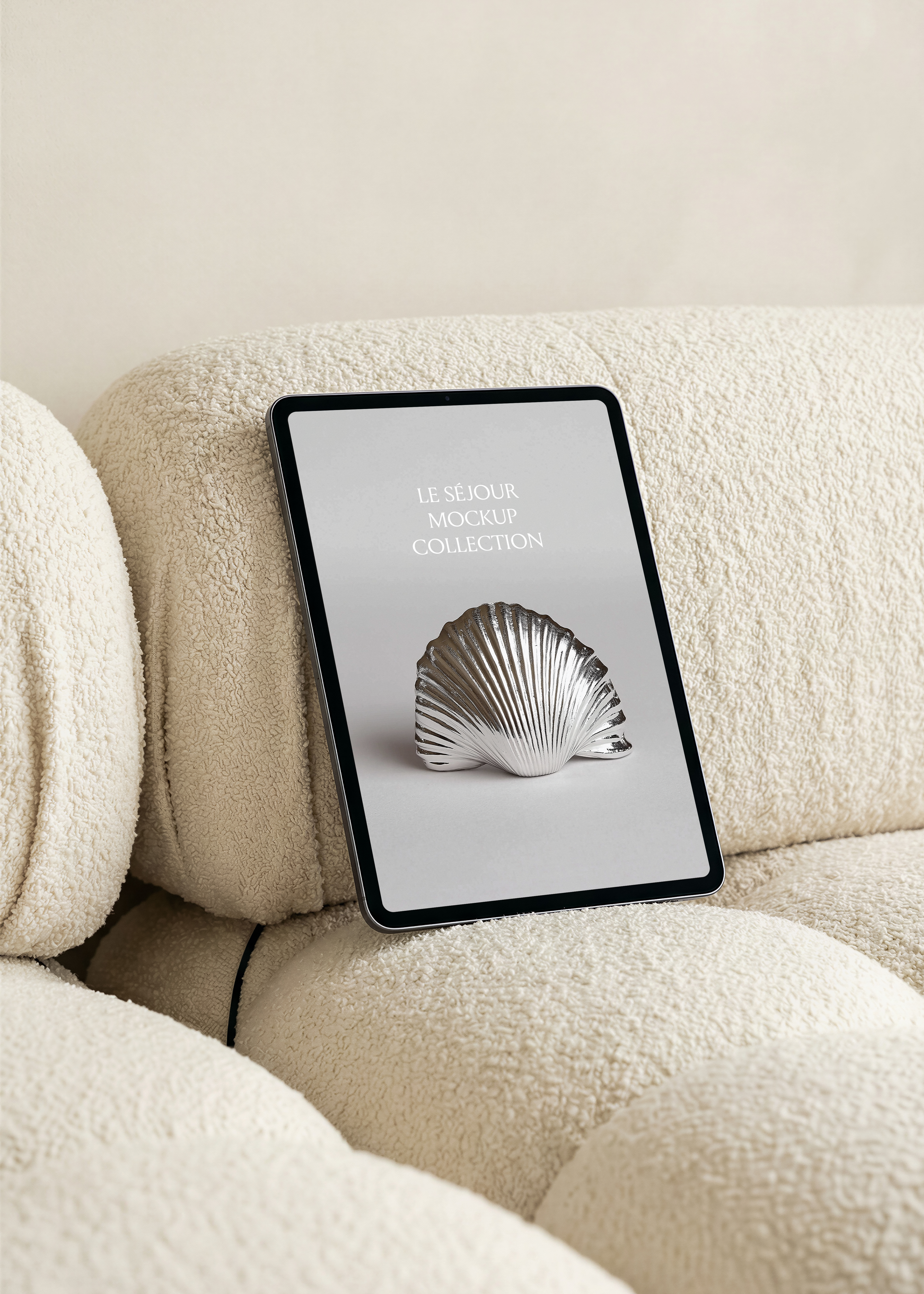 Portrait iPad mockup leaning against the back cushion of a cream boucle modular sofa, warm neutral wall behind