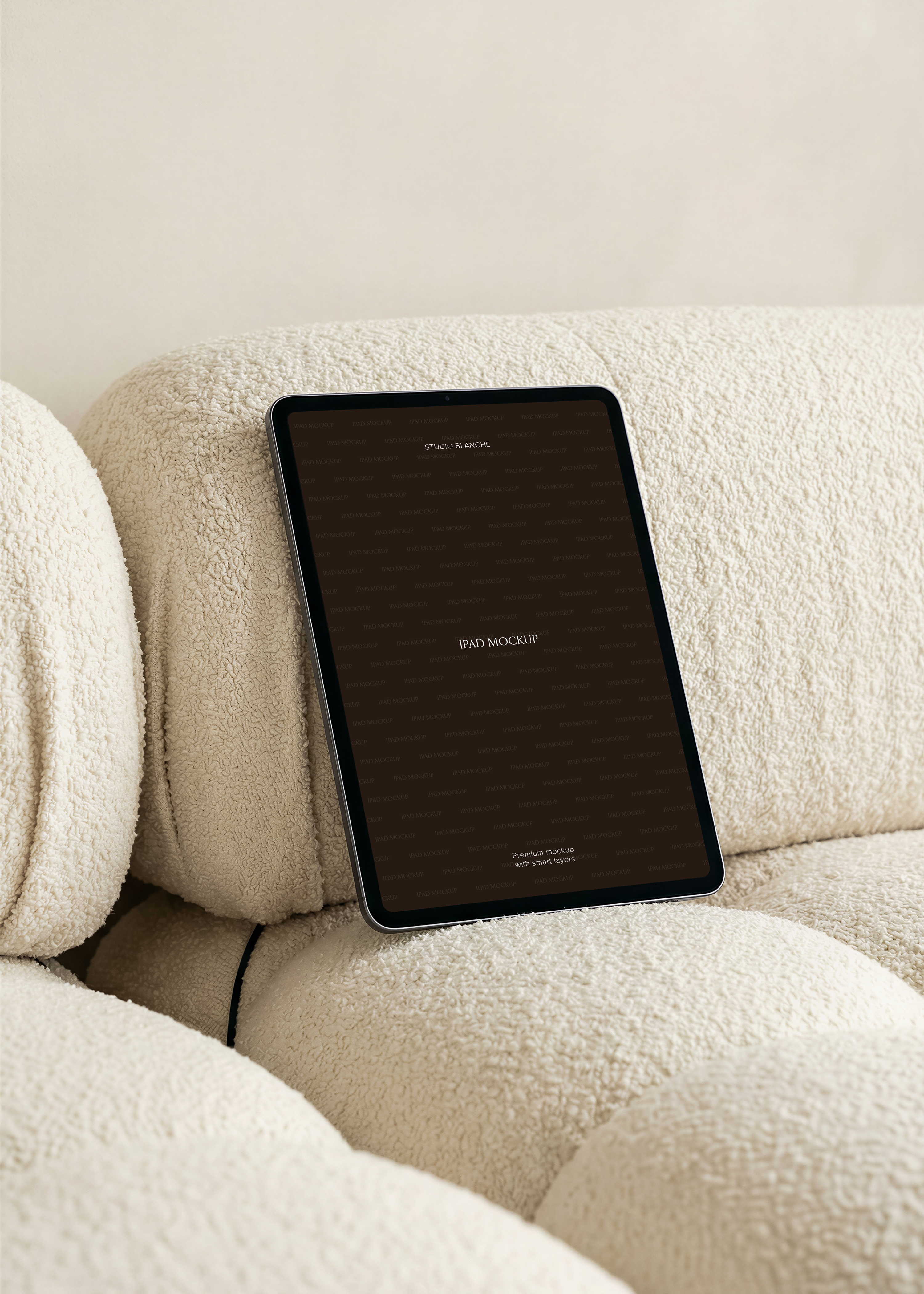 iPad mockup detail of a dark tablet screen resting on textured cream boucle upholstery, rounded cushions in soft light