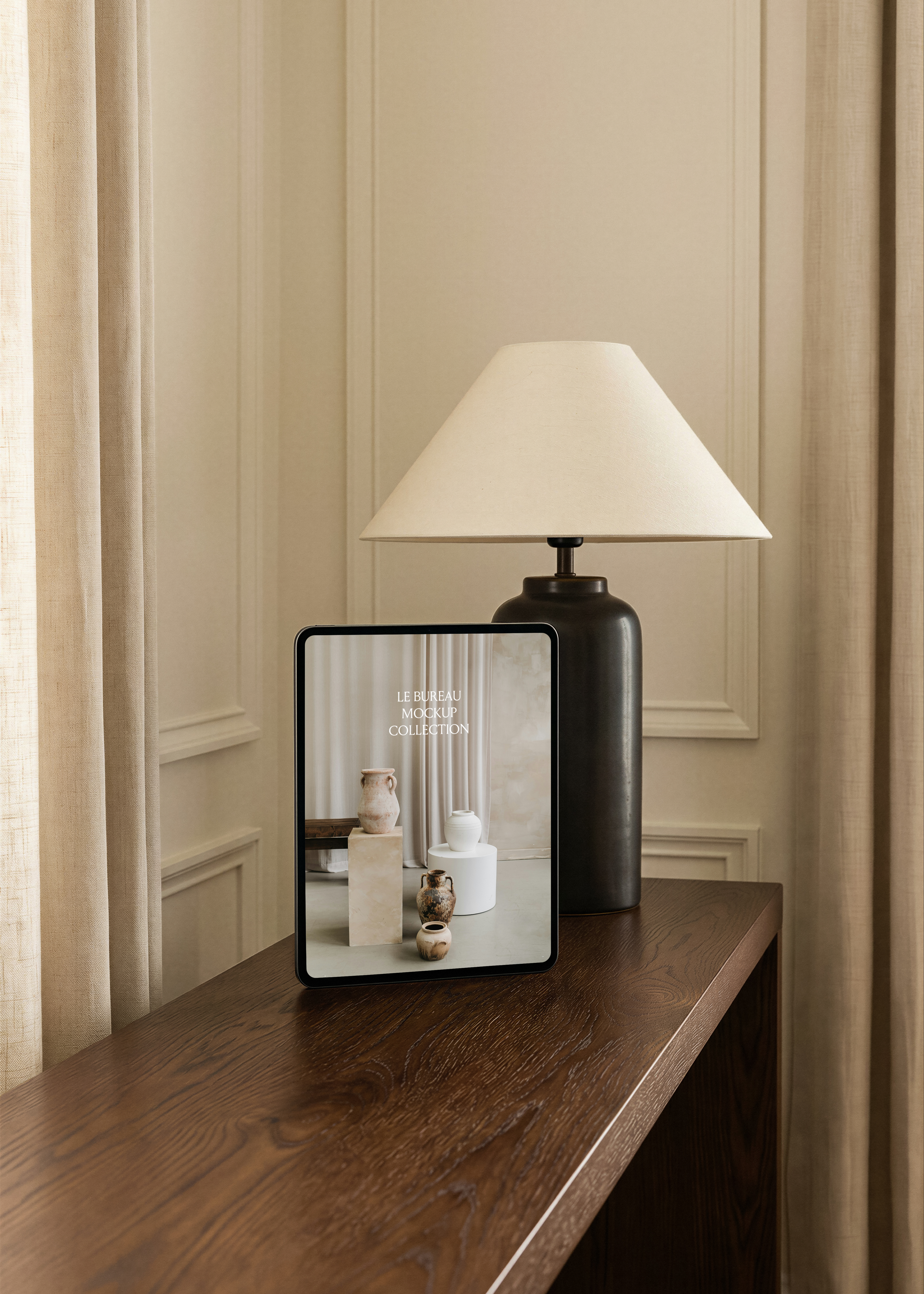 iPad mockup displaying Le Bureau editorial on dark oak console, charcoal lamp and linen curtain, panelled room backdrop