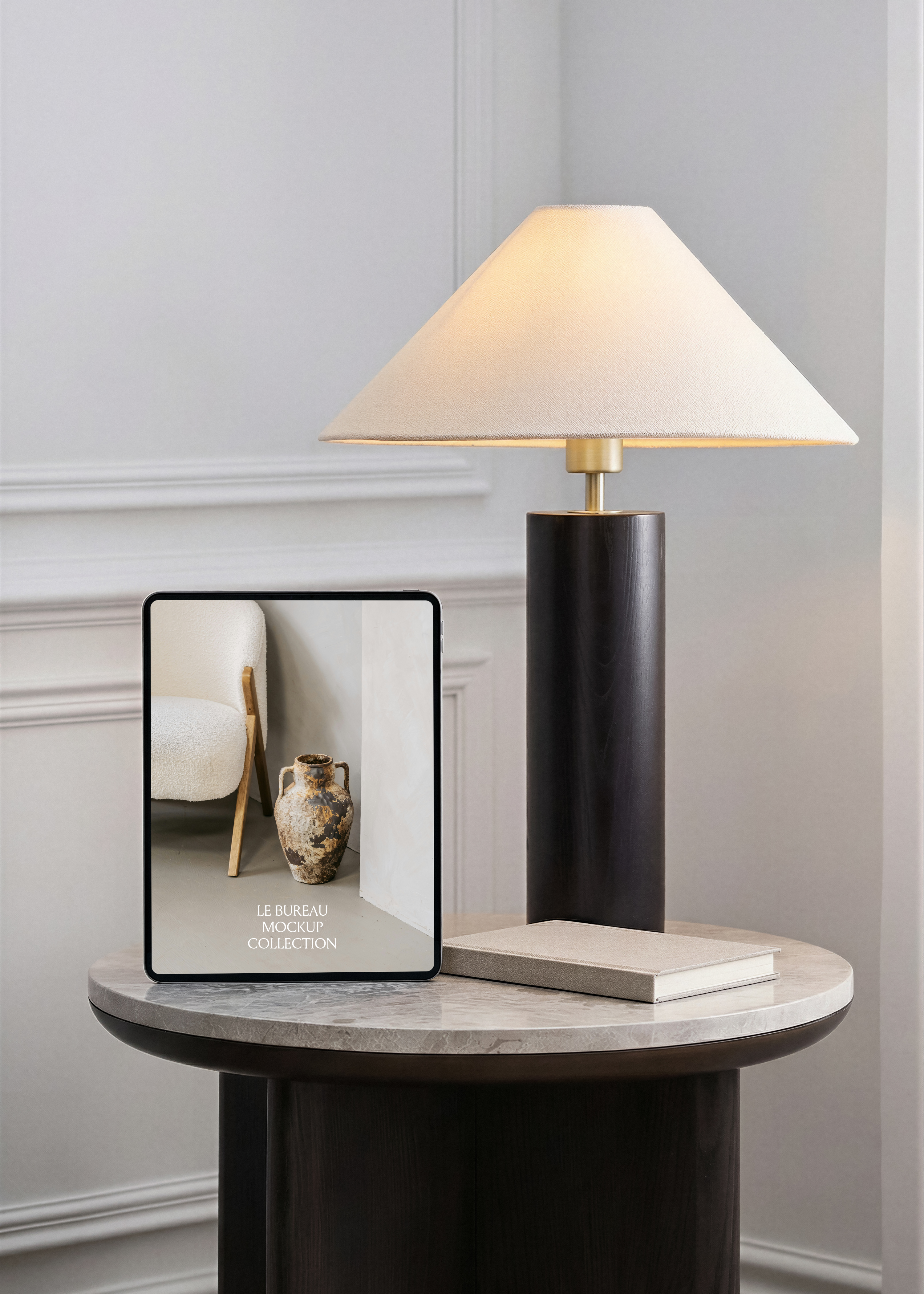 iPad mockup displaying Le Bureau editorial on marble side table, dark column lamp with cream shade and panelled wall 