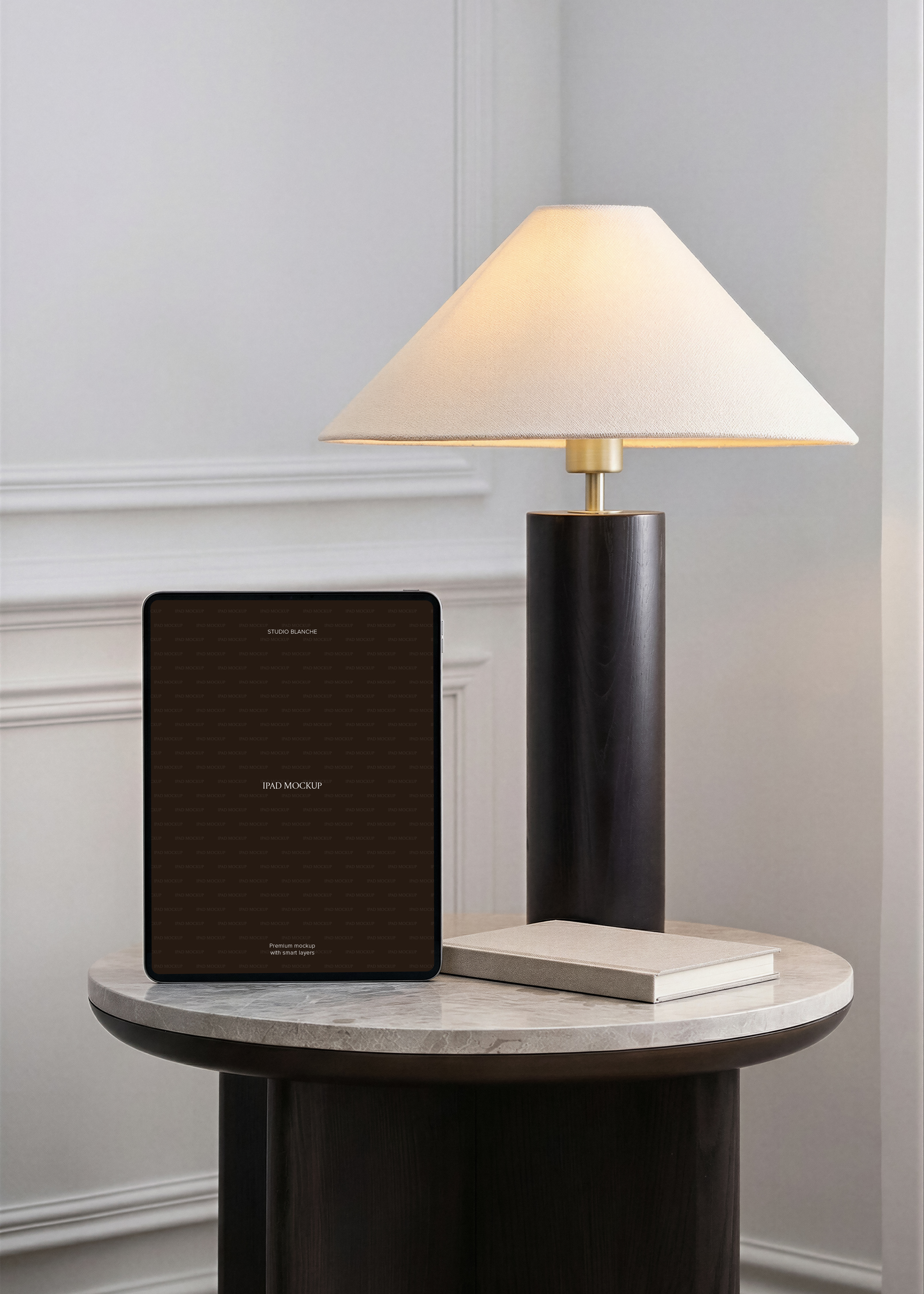 iPad mockup in portrait on marble-top side table beside dark cylindrical brass lamp, dove-grey panelled wall interior 