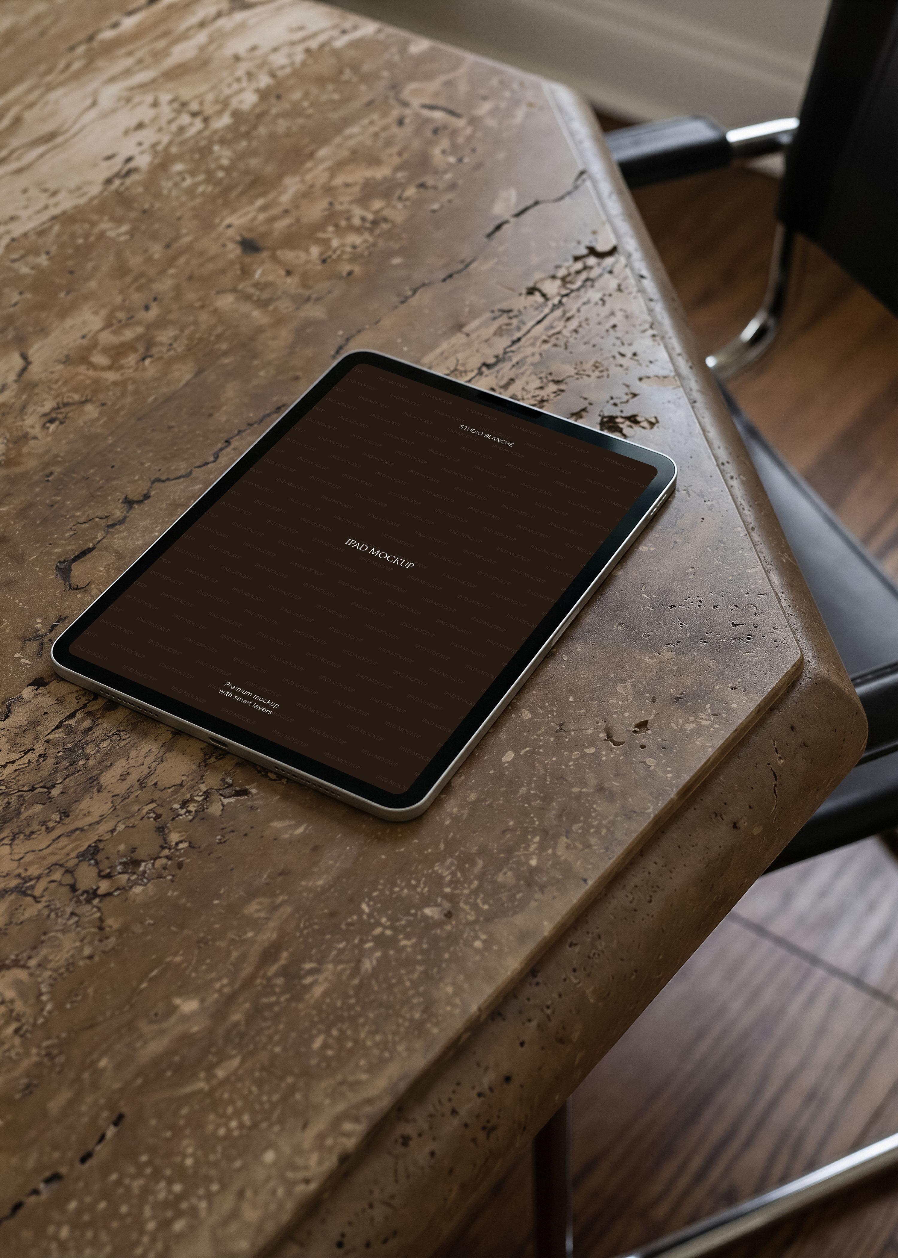 iPad mockup resting at an angle on textured travertine desk beside chrome and leather chair legs, warm tones