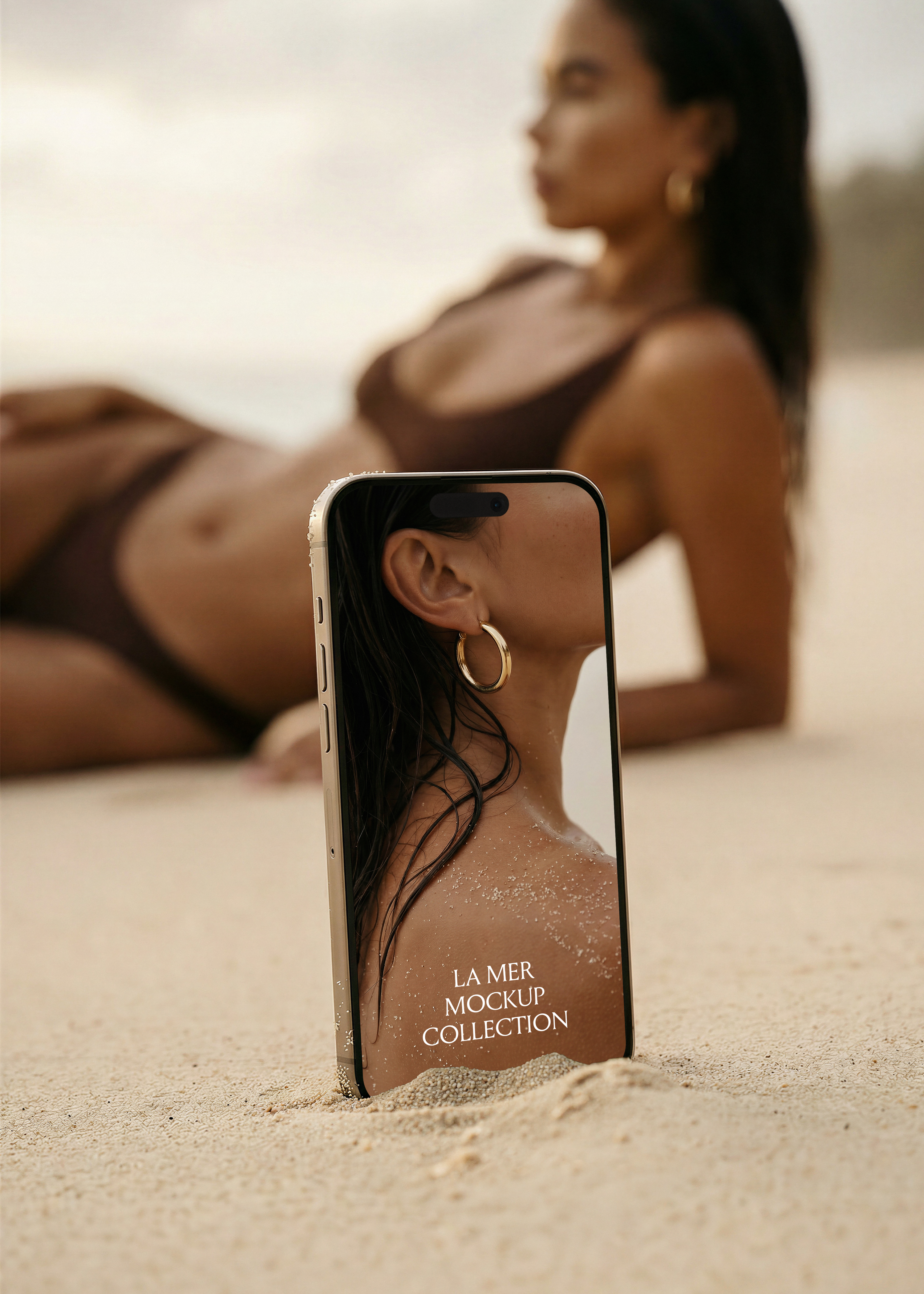 iPhone mockup standing in beach sand at ground level, editorial swimwear lifestyle scene in background, gold frame