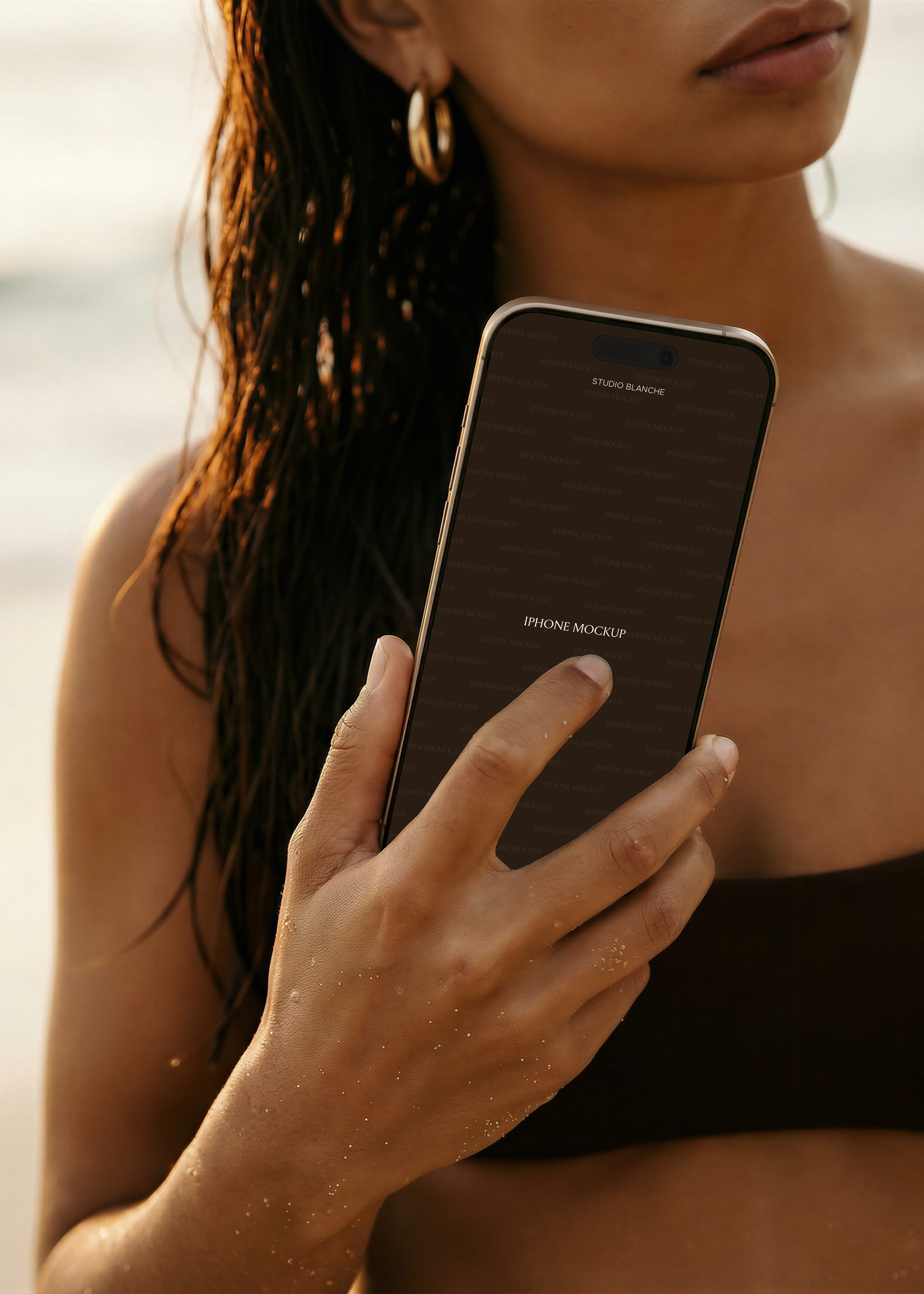 Beach iPhone mockup held in model's hand against dark bikini top, warm amber light, dark screen placeholder