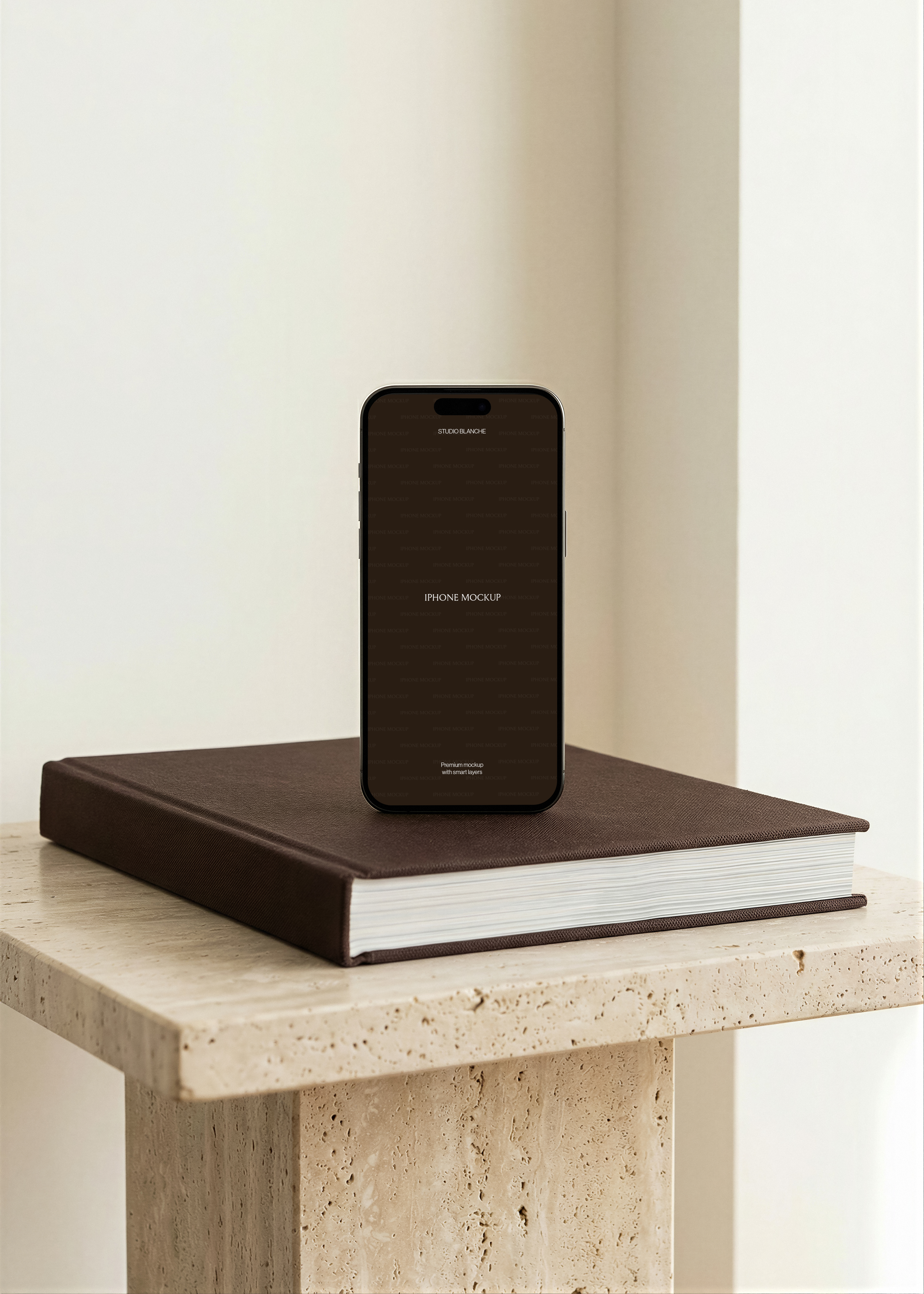 iPhone mockup upright on dark cloth-bound hardcover book atop travertine plinth, minimal white interior backdrop
