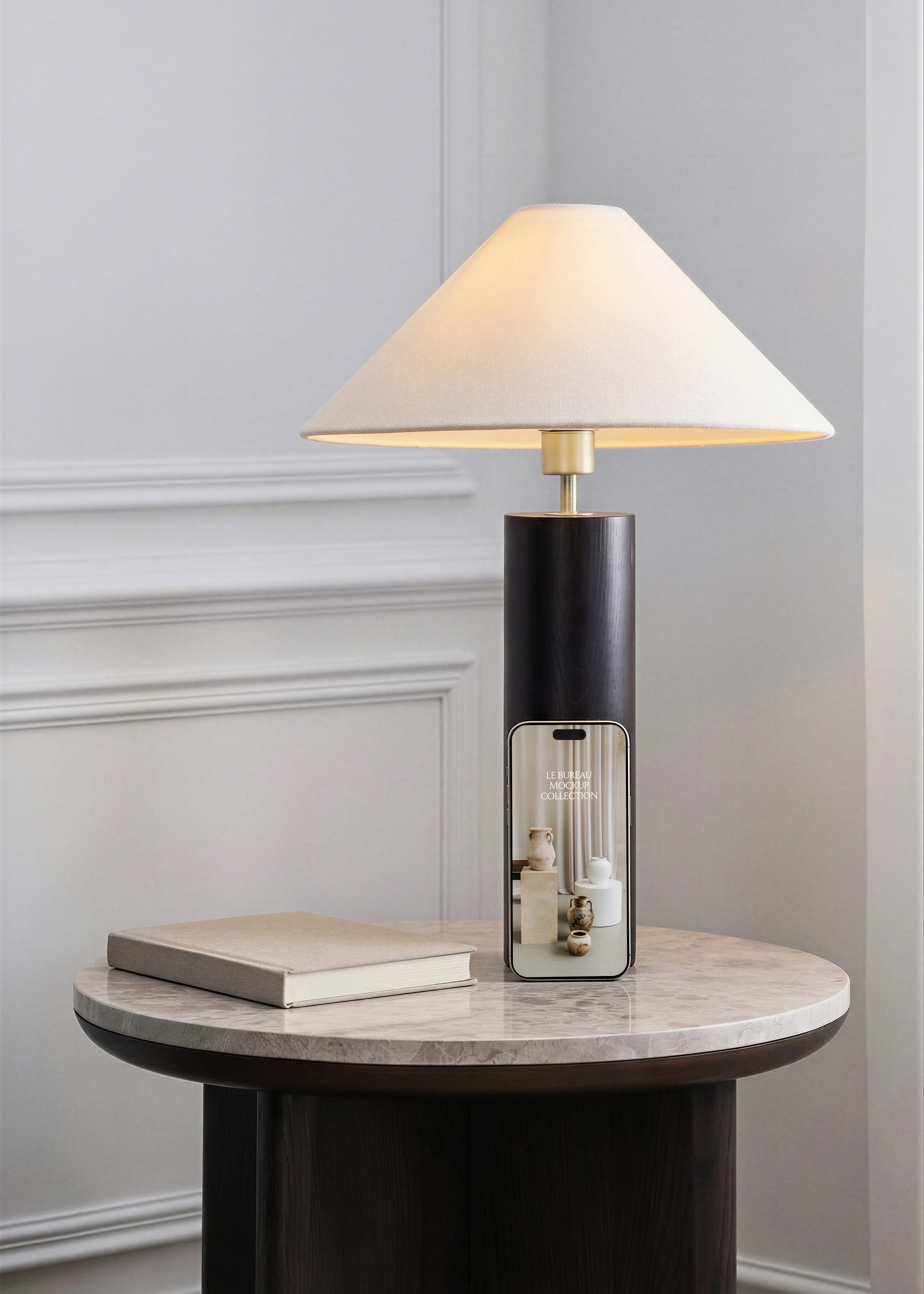 iPhone mockup displaying Le Bureau editorial against dark column lamp on marble table, linen notebook and grey panelled wall 